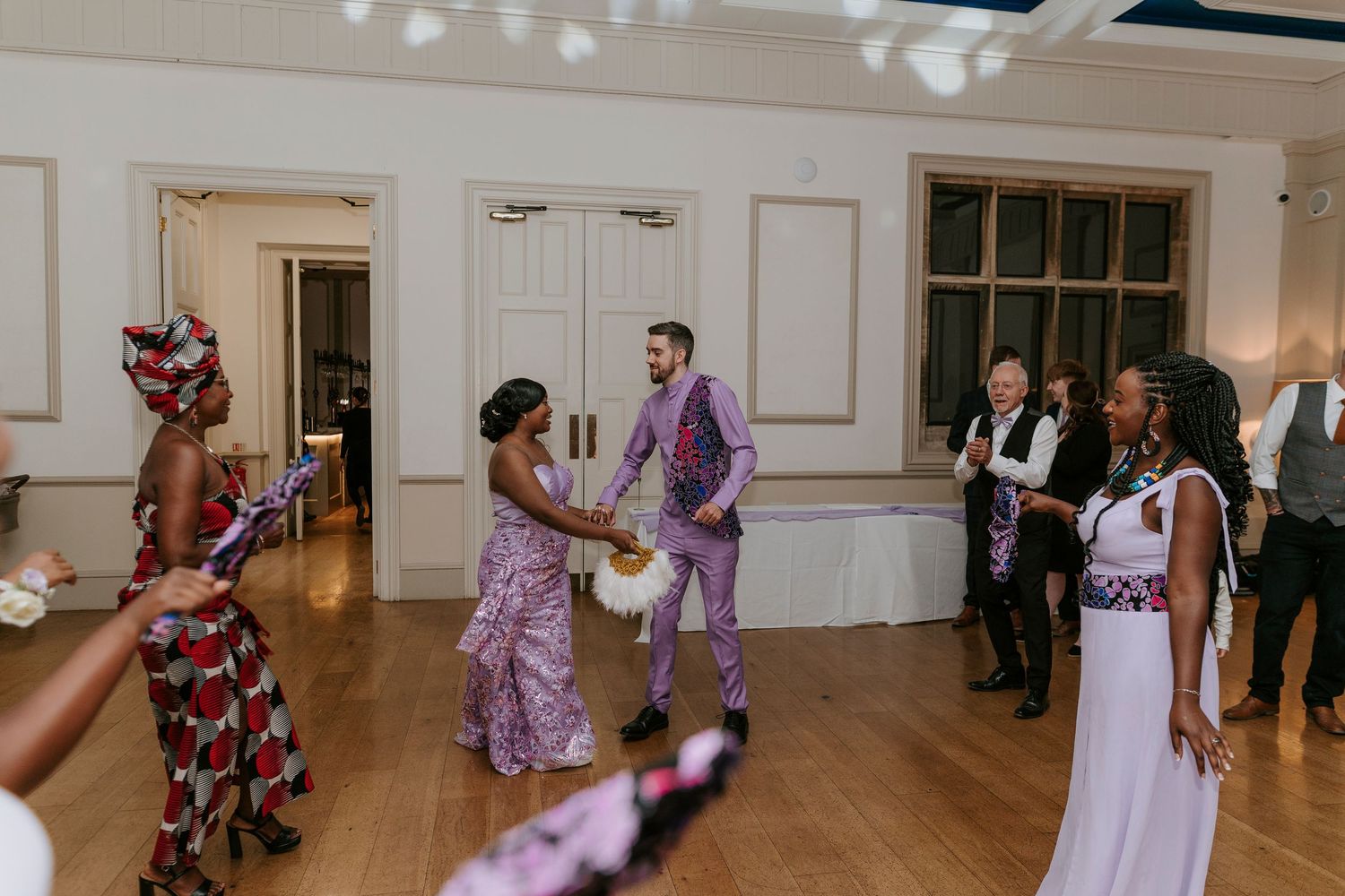 Wedding guests dance and celebrate together on a white-walled ballroom dance floor during a reception.