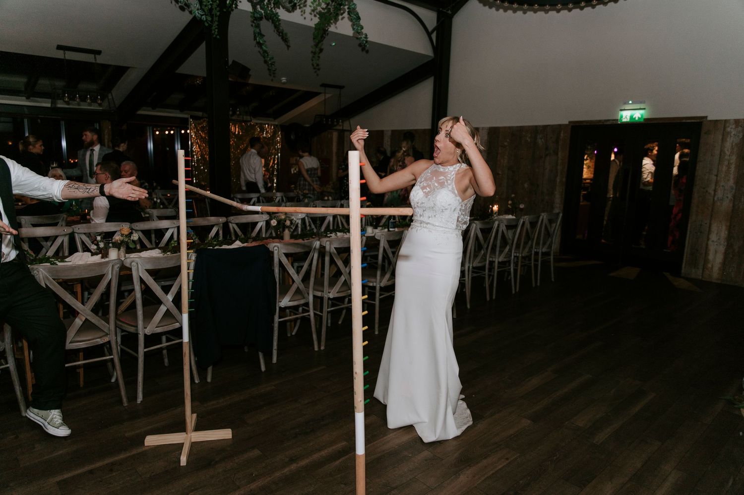 People dance and celebrate at a wedding reception on a dark wooden dance floor with string lights overhead.