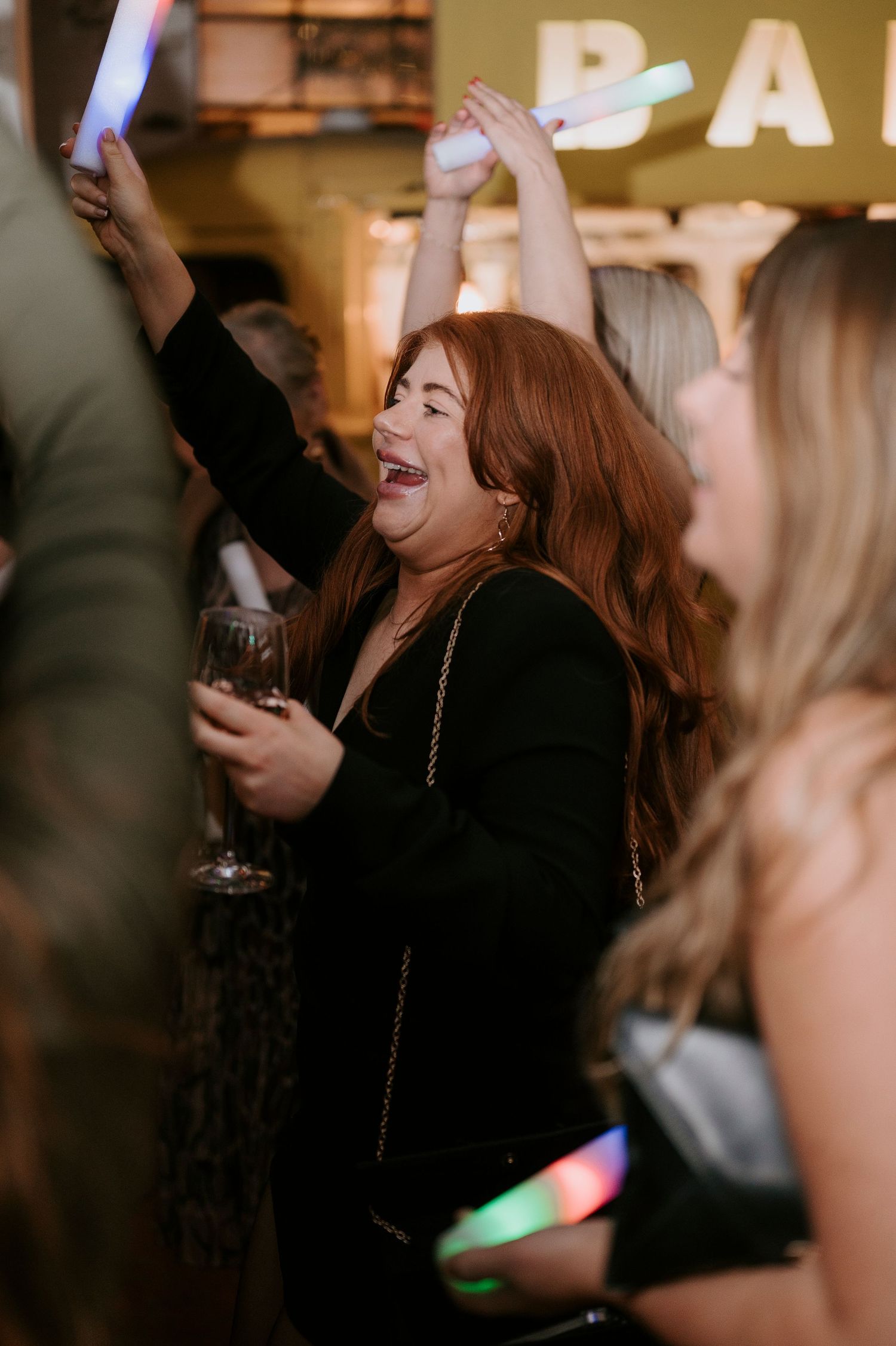 Joyful woman with red hair dancing with glow sticks at lively wedding reception party.