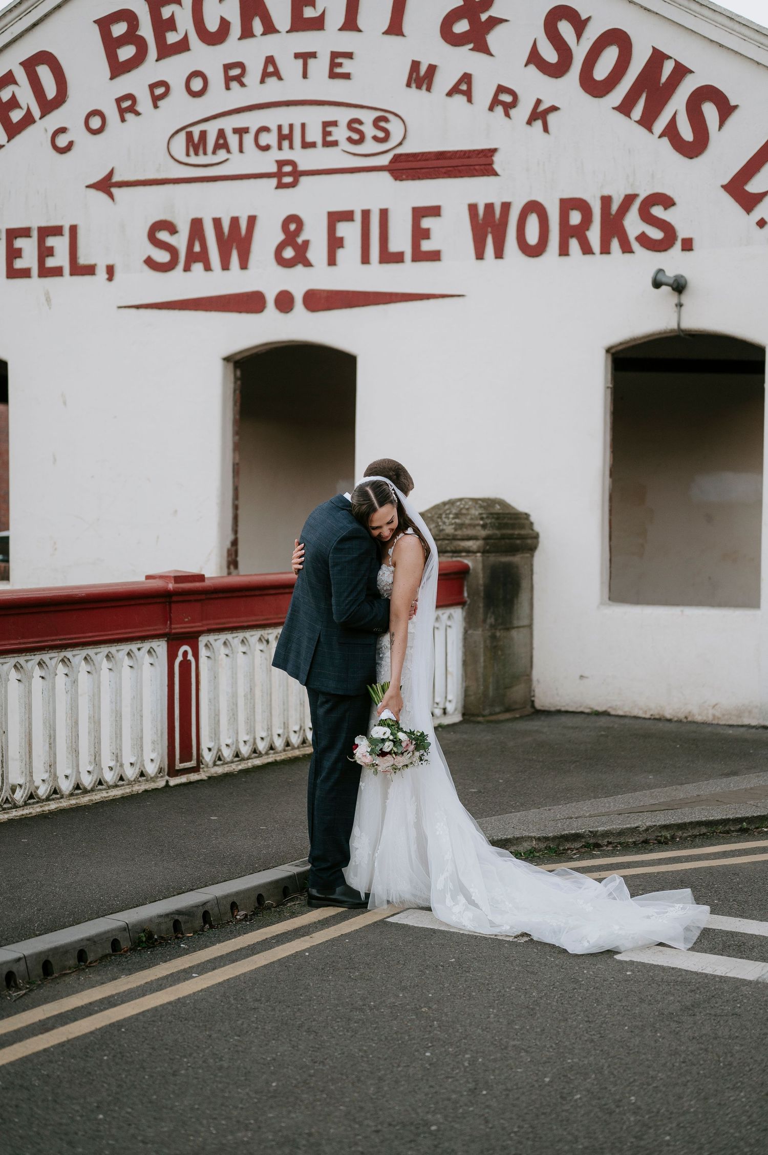 Bride and groom share a romantic kiss outside Beckett & Sons Steel Saw & File Works building on their wedding day.