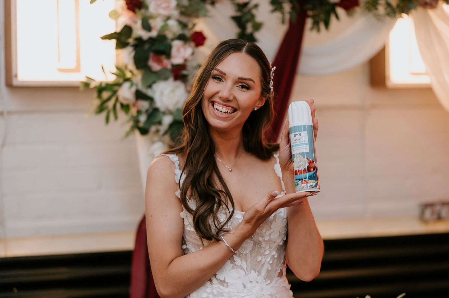 Happy bride in lace gown smiling while holding a product during wedding ceremony.