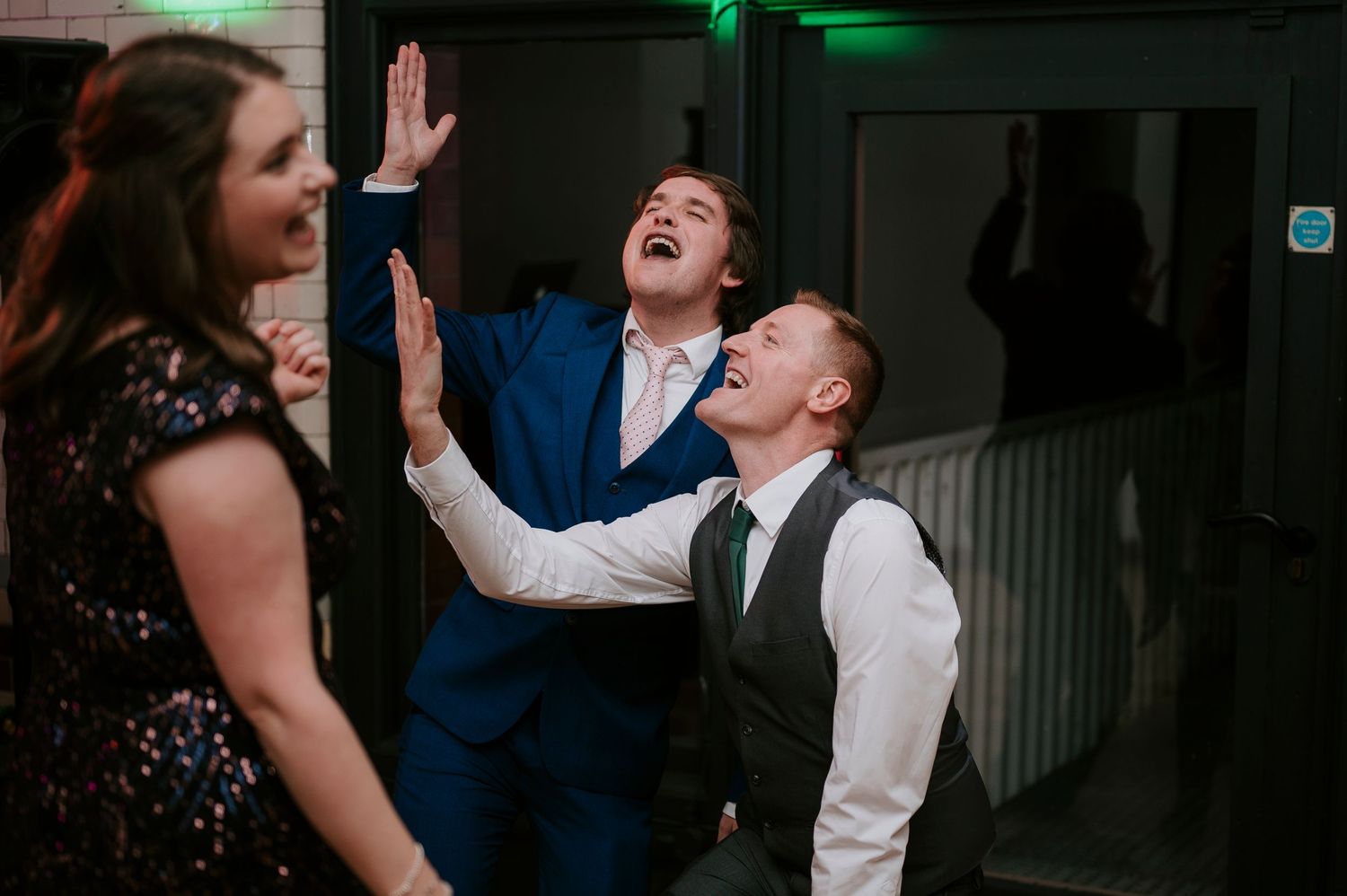 Wedding guests share joyful dancing moments under atmospheric green lighting.