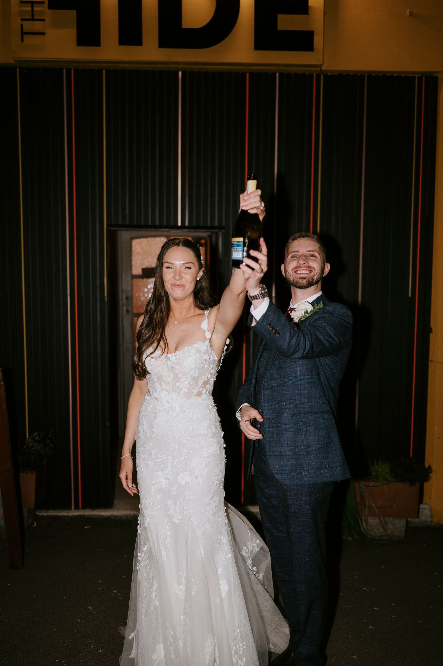 Newlyweds raise a champagne bottle in celebration outside The Hide venue after their wedding.