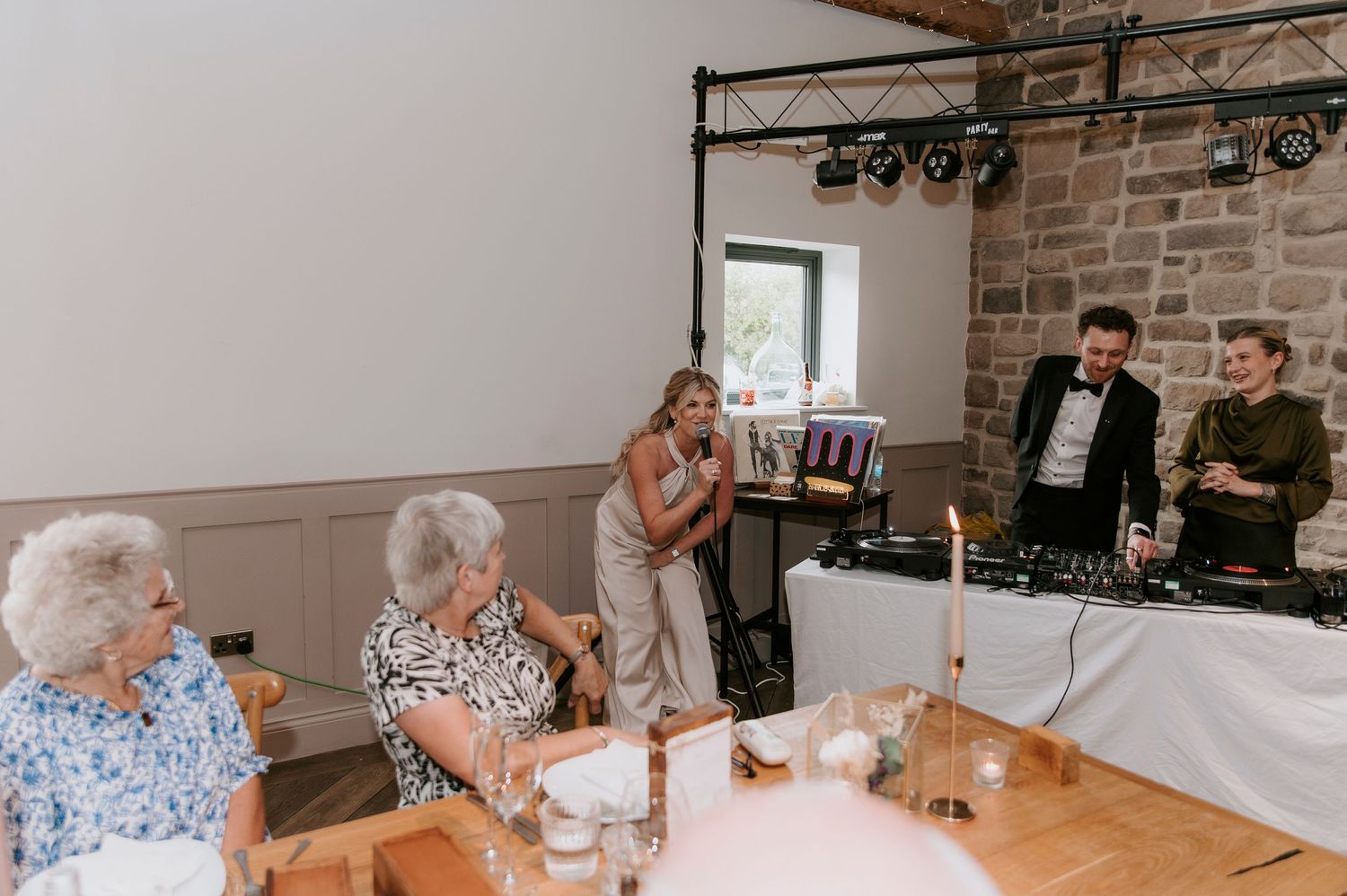 People gather around tables for a social event in a bright room with exposed brick walls and white decor.