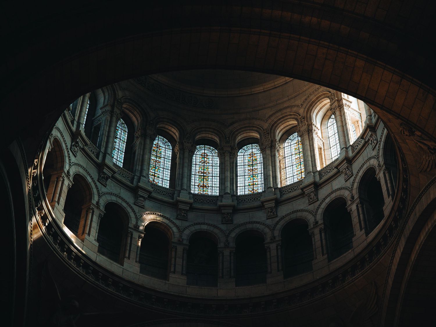Interior view of a grand cathedral dome with arched stained glass windows and ornate stone architecture.
