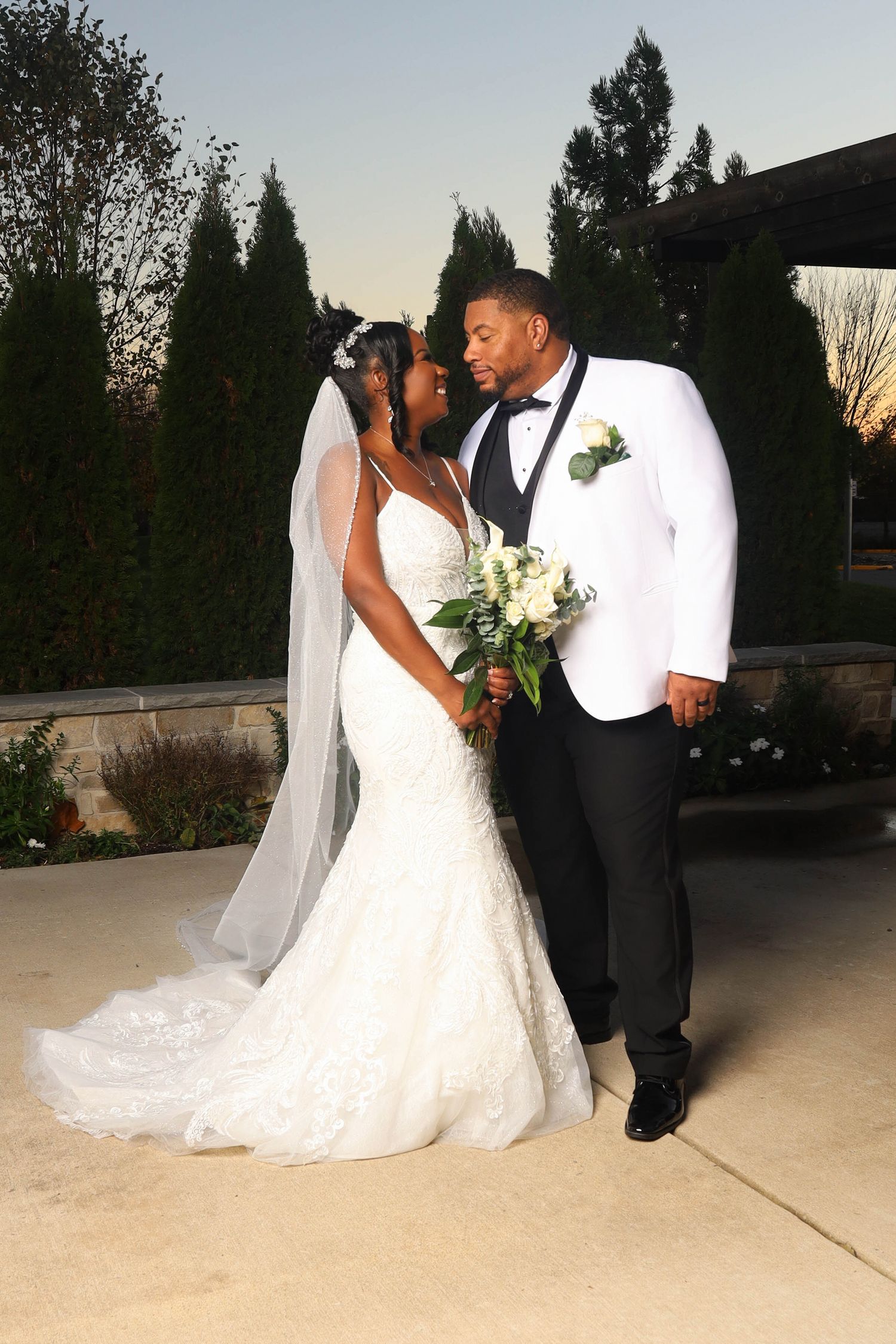 Bride and groom share a romantic moment outdoors, bride in lace mermaid gown with veil.