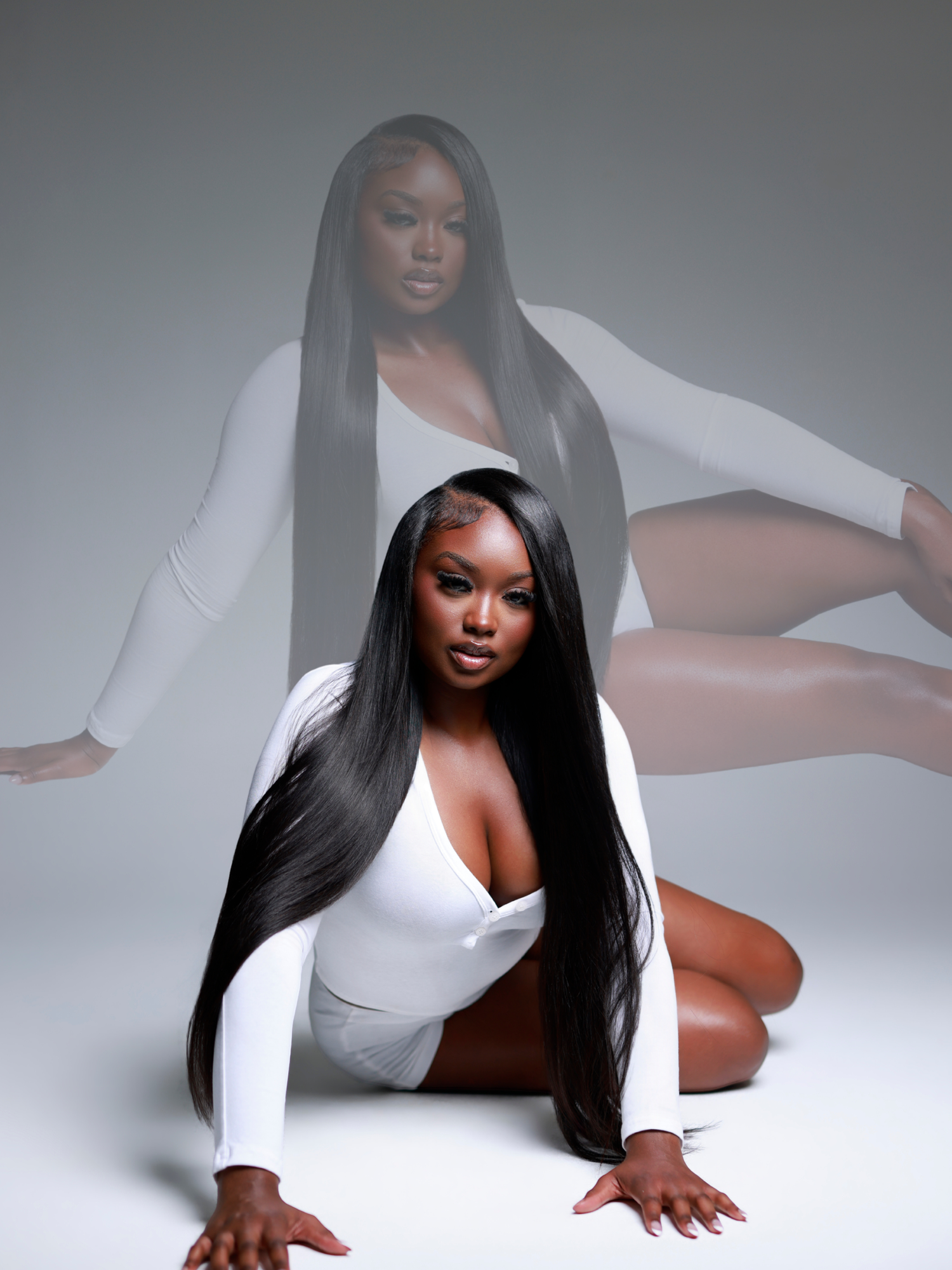 A Black woman in a white bodysuit poses on the floor with long straight hair, with a ghosted image behind her.