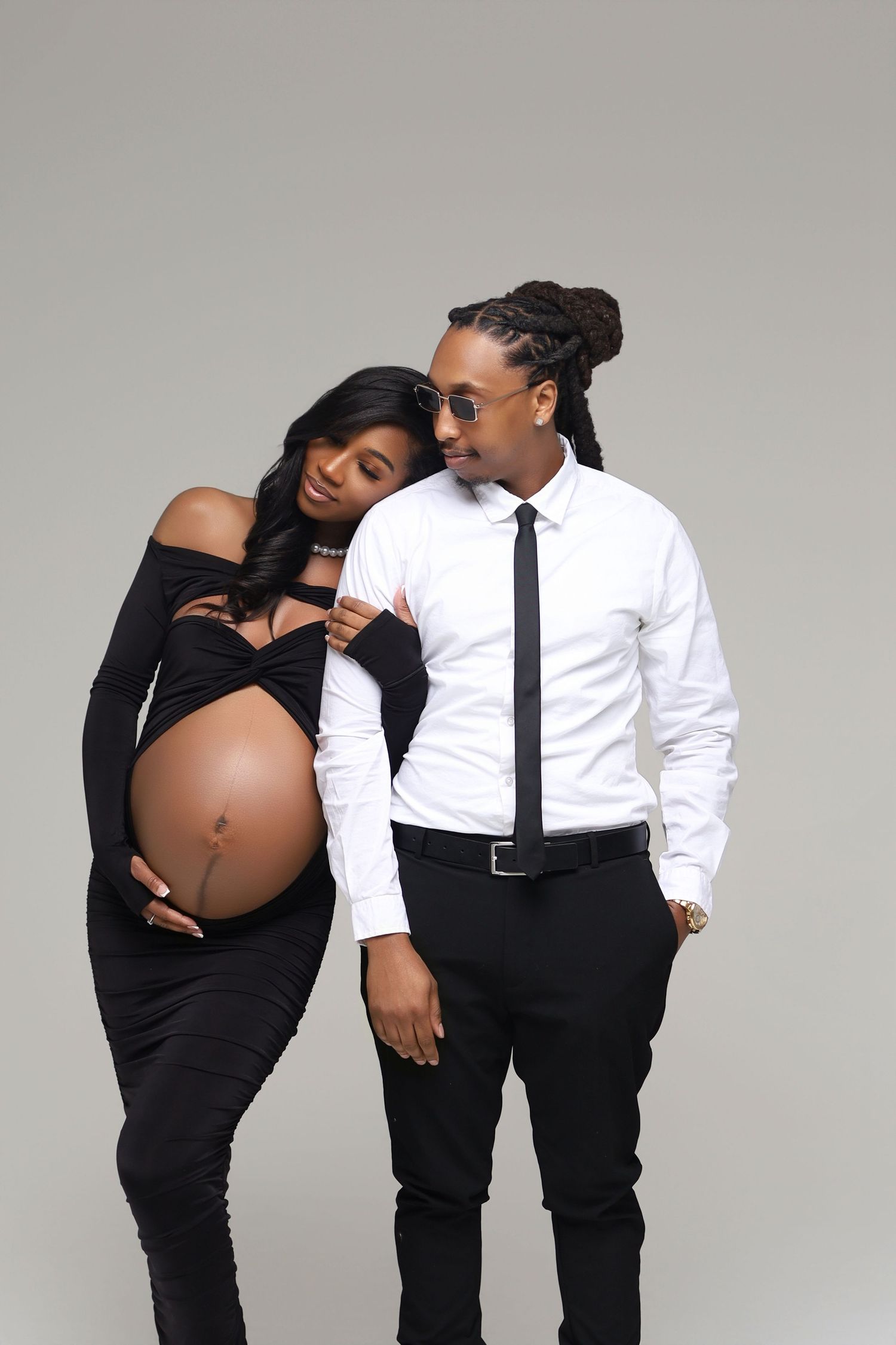 Pregnant couple in black and white outfits poses together in a stylish studio maternity portrait.