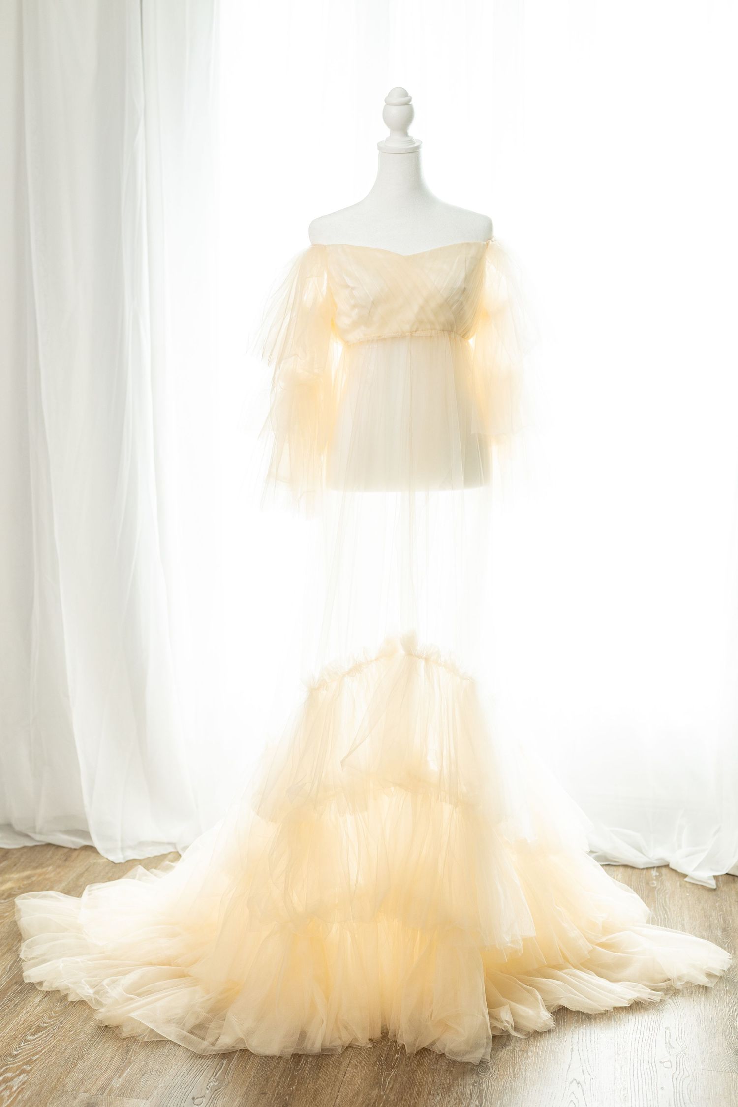 Elegant champagne tulle off-shoulder wedding gown with ruffled layers and train displayed on a mannequin.