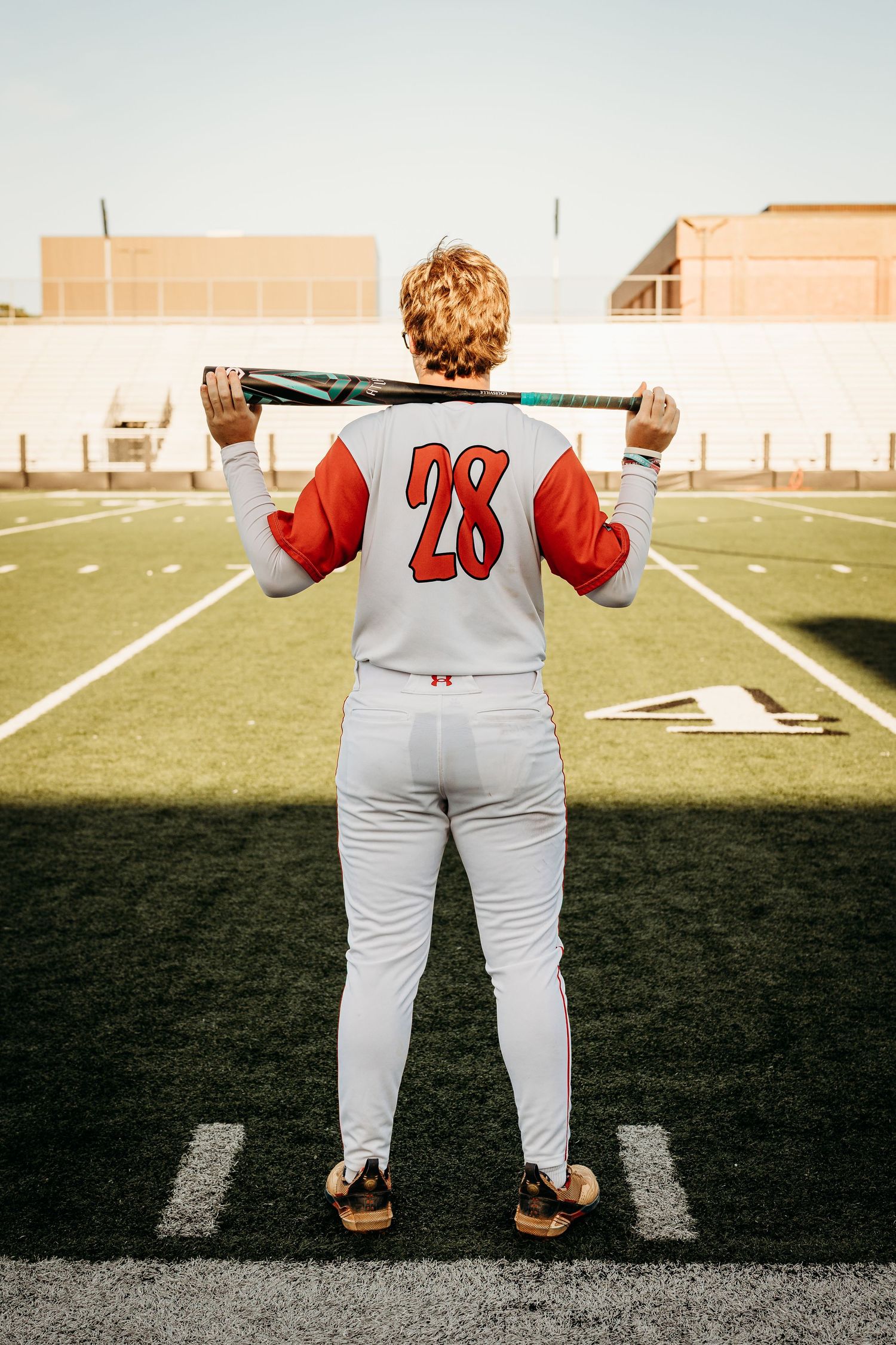 Baseball player wearing number 28 jersey stands on field holding bat behind shoulders.