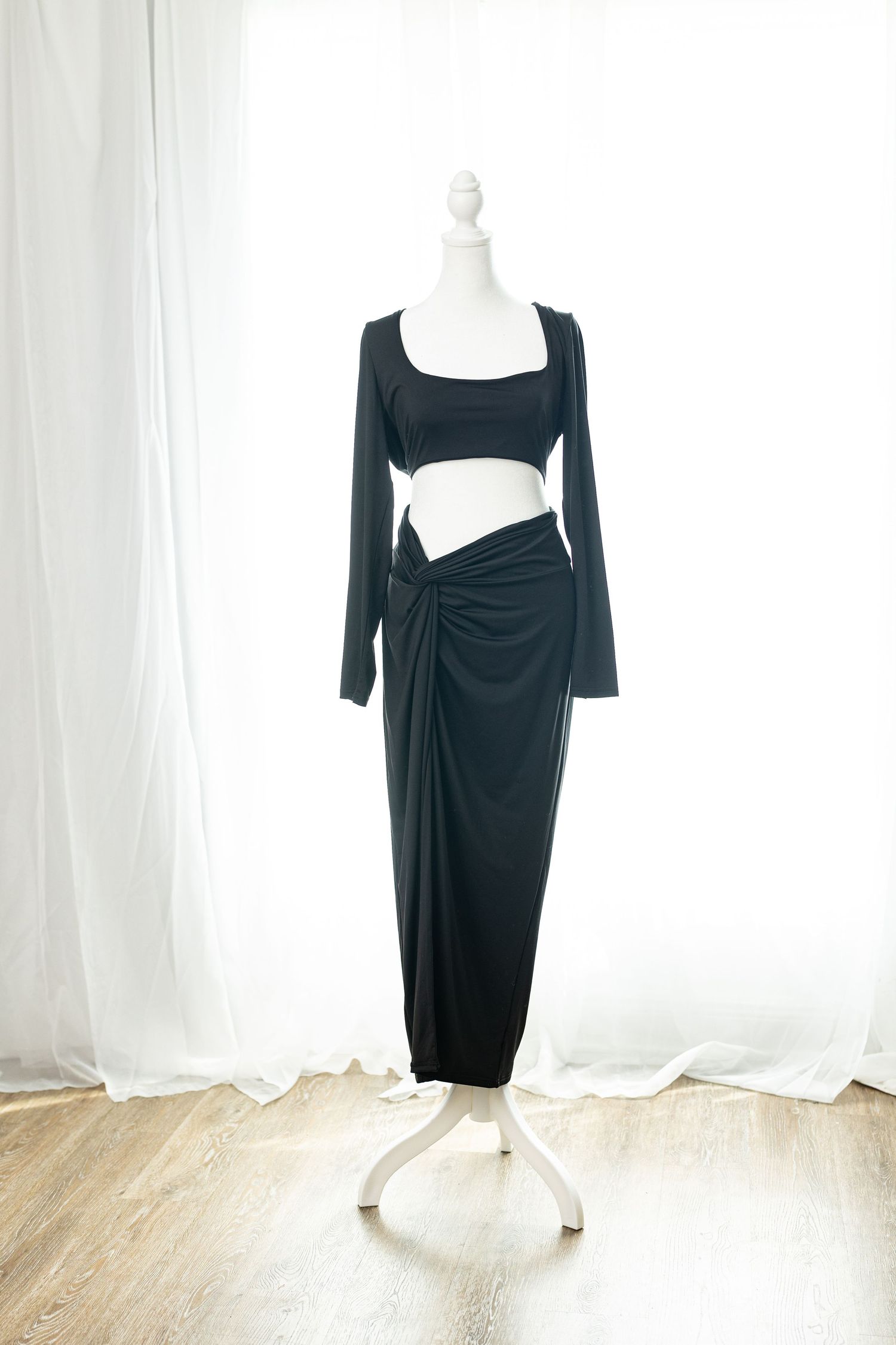 Black two-piece set featuring a long-sleeve crop top and ruched maxi skirt displayed on a mannequin.