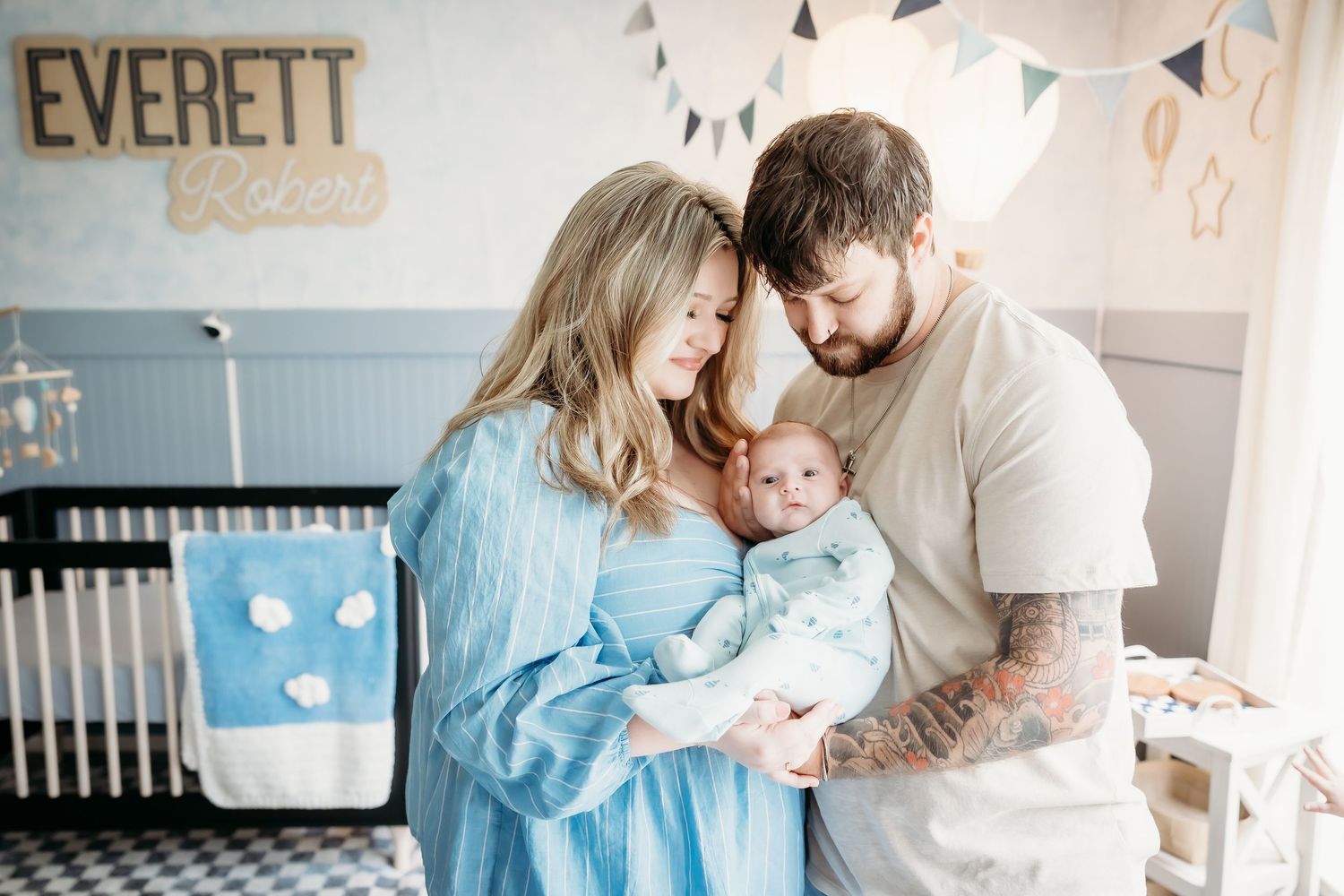 New parents tenderly holding newborn baby in nursery decorated with name sign Everett.