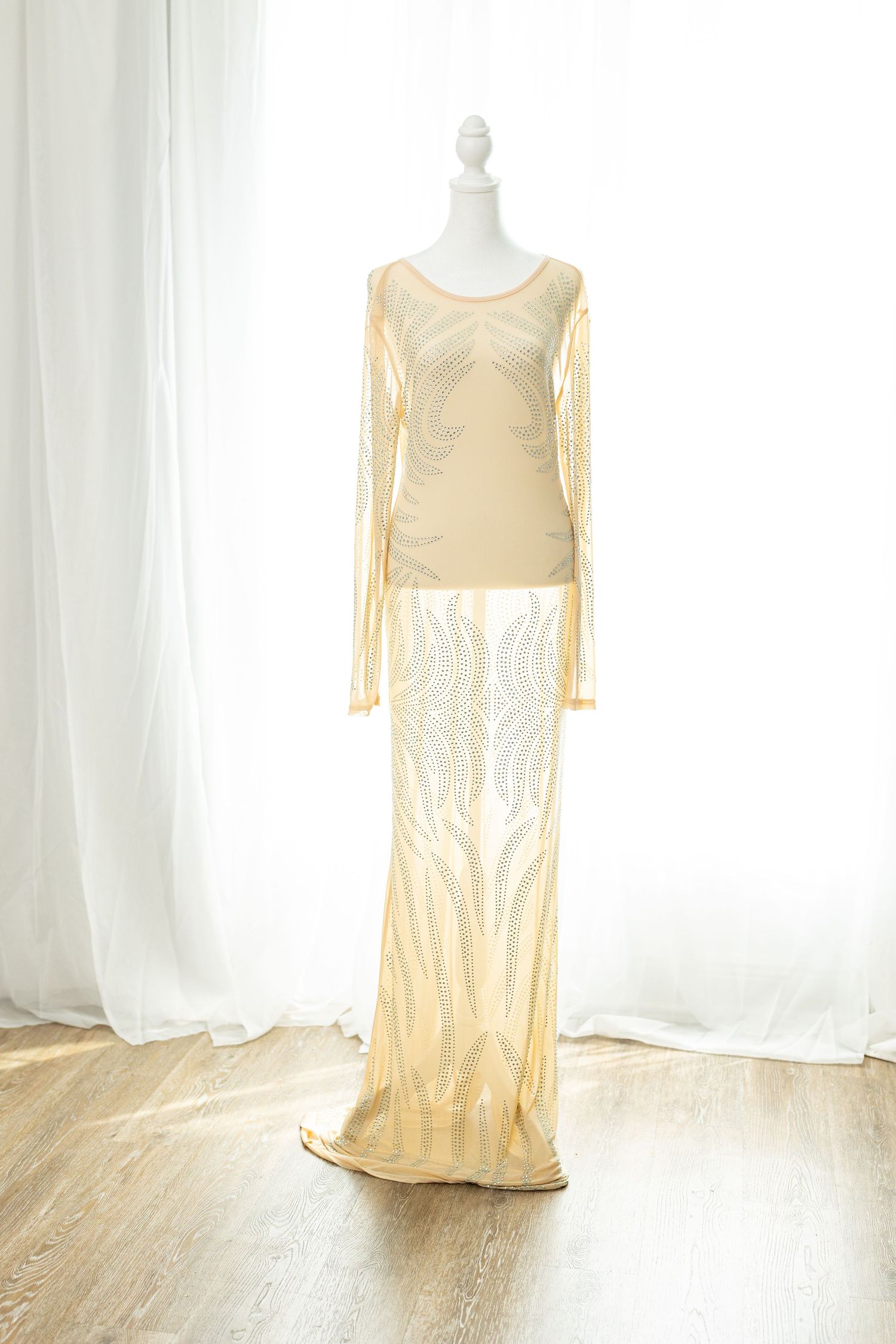 Elegant gold sheer lace maxi dress with long sleeves and intricate pattern on mannequin.