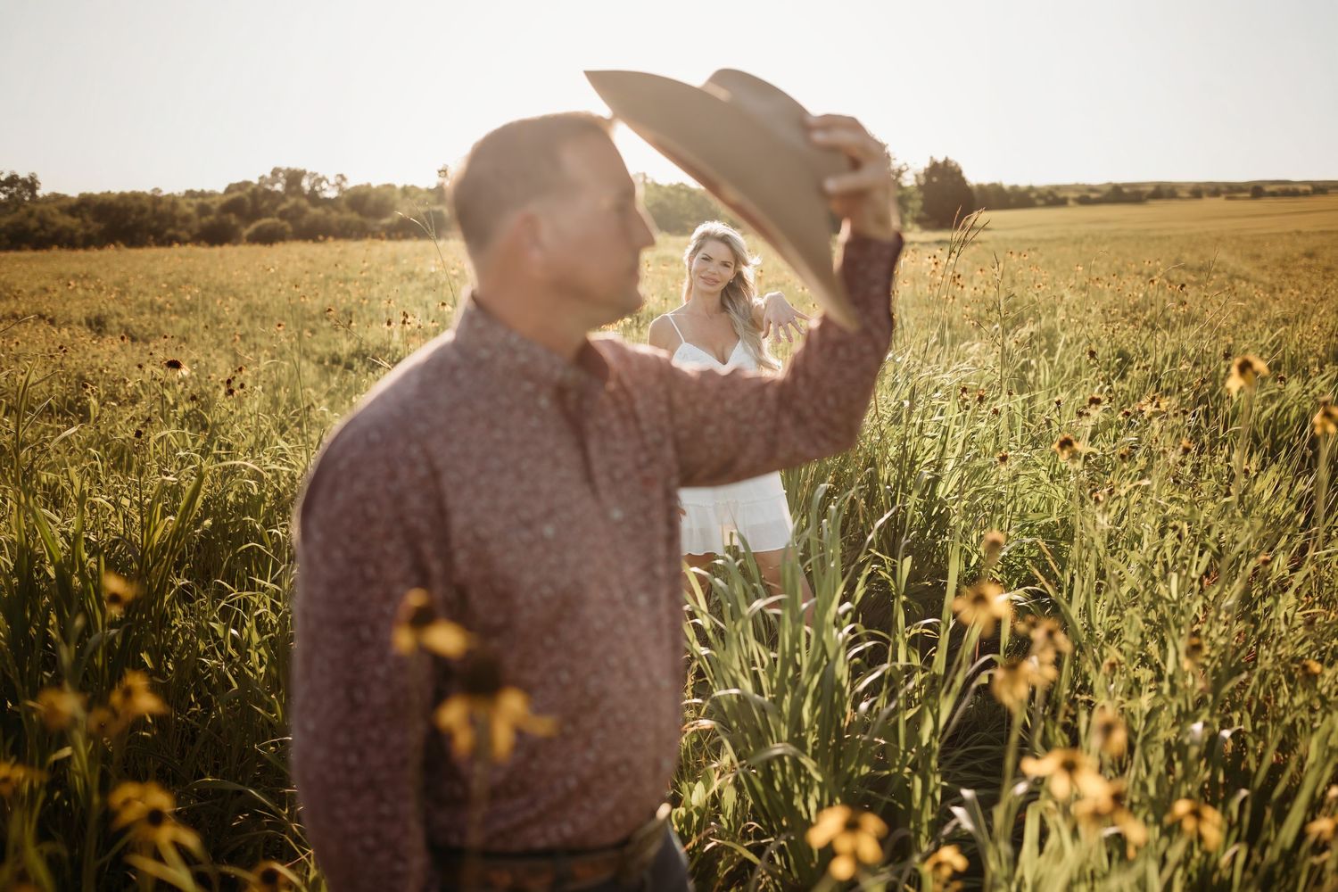 Man in cowboy hat tipping his hat toward smiling woman in a sun-drenched wildflower field.