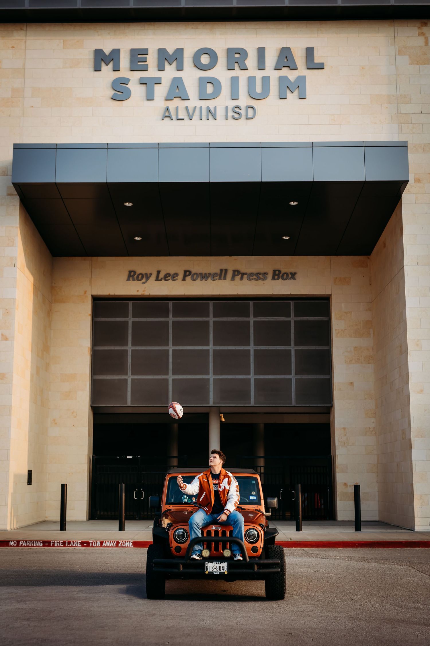 Teen boy tosses football on Jeep hood outside Memorial Stadium Alvin ISD for senior photos.