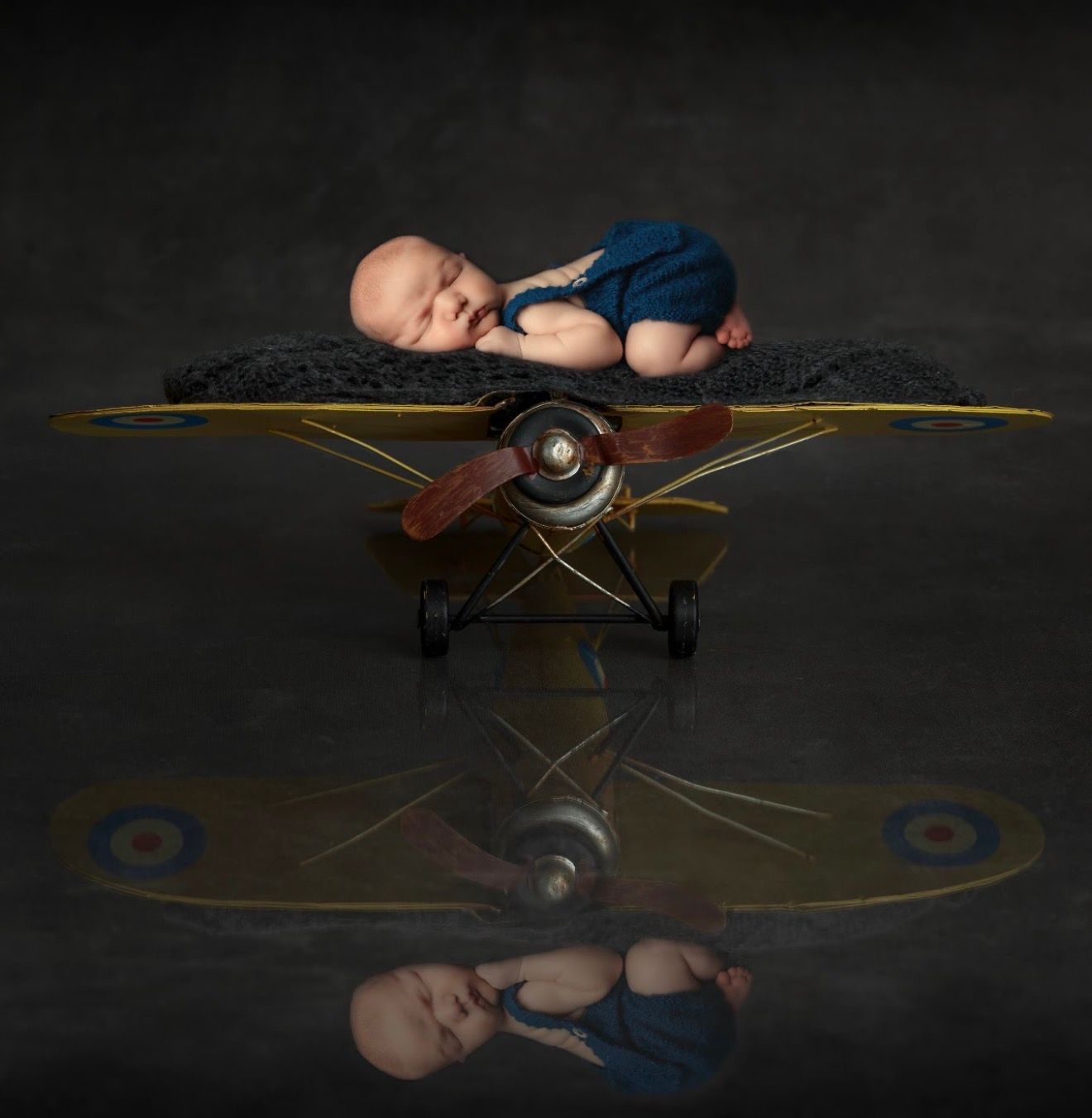 Newborn baby sleeping peacefully on a vintage toy airplane with a beautiful reflection below.