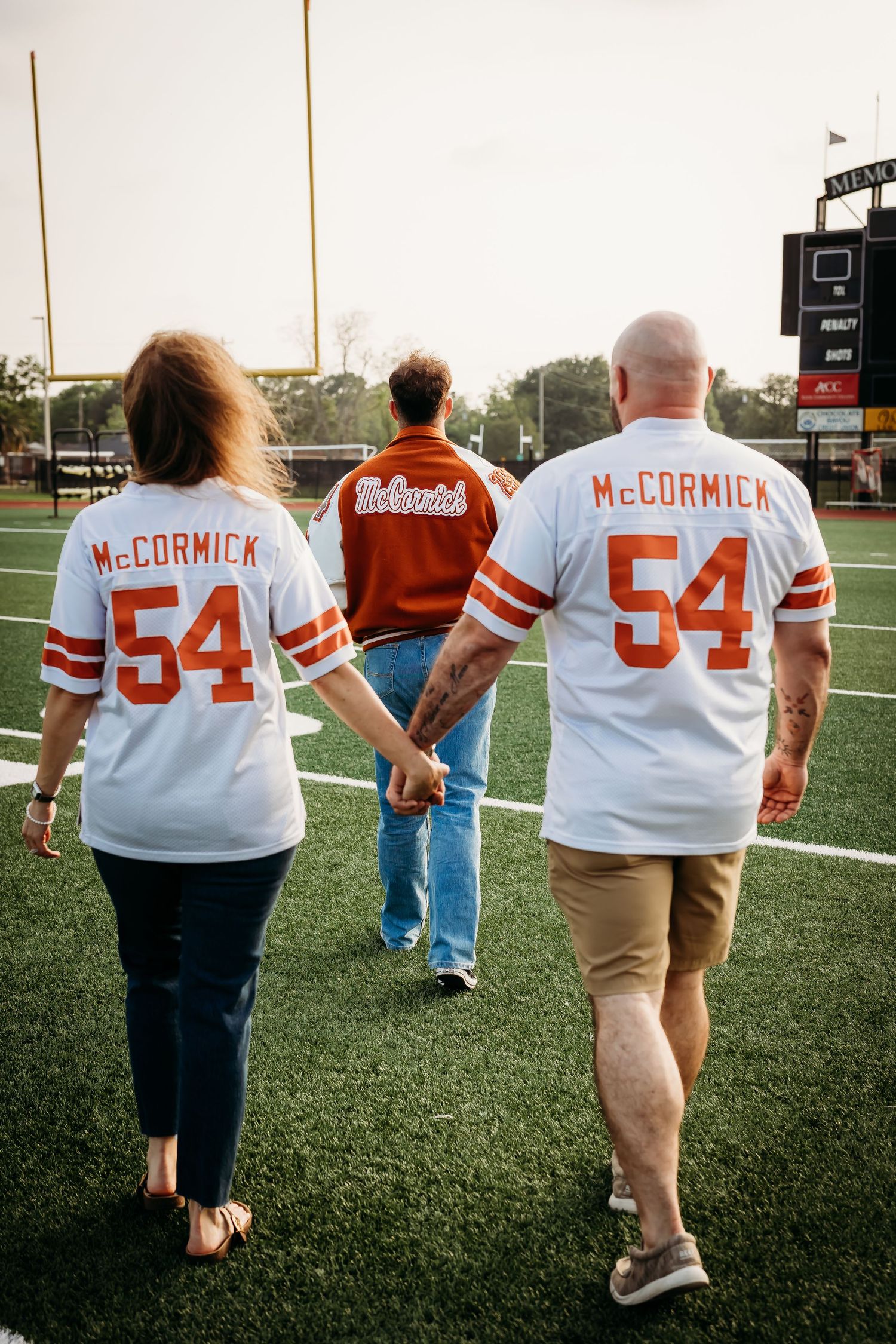 Parents in matching McCormick 54 jerseys walk with graduate on football field.