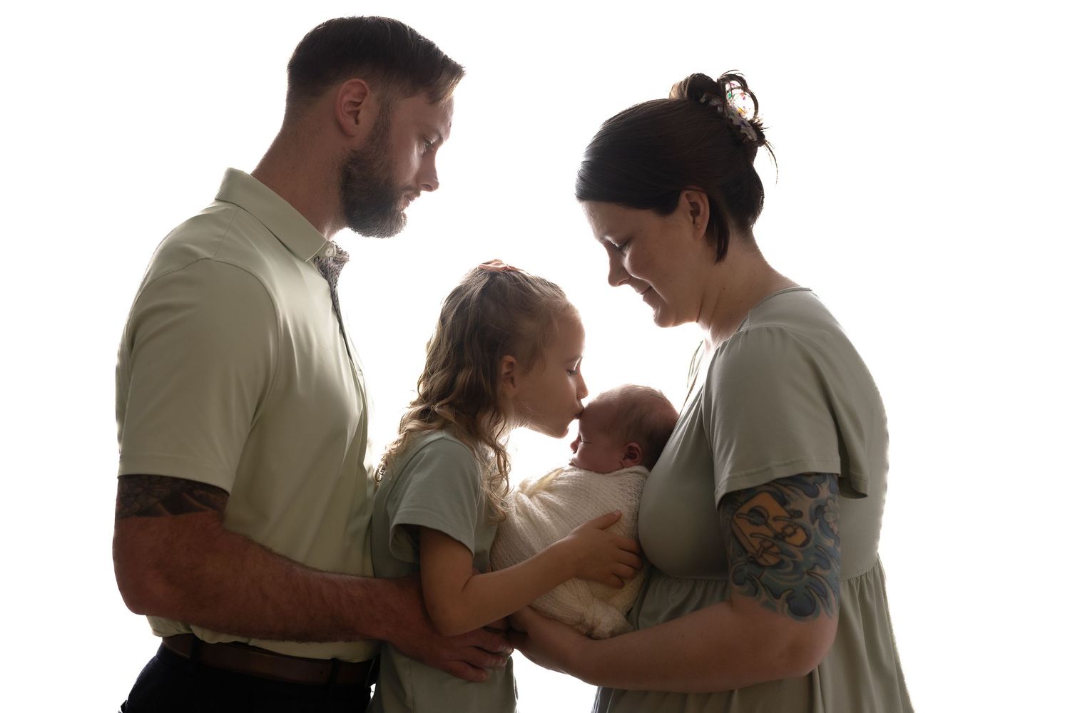 Family of four with tattooed father, mother, young daughter, and newborn baby in white studio.