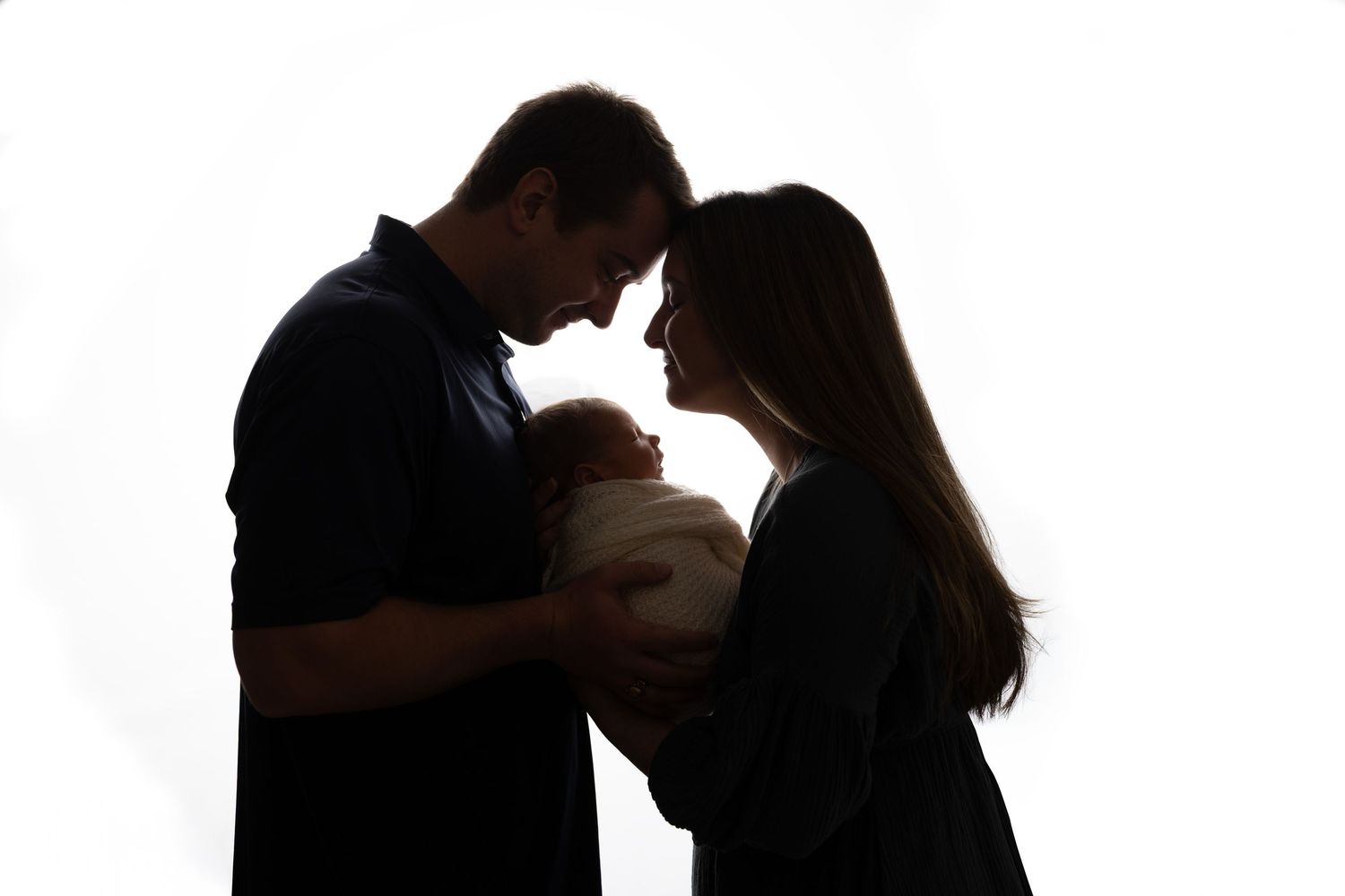 Silhouette of parents holding newborn baby against white background.