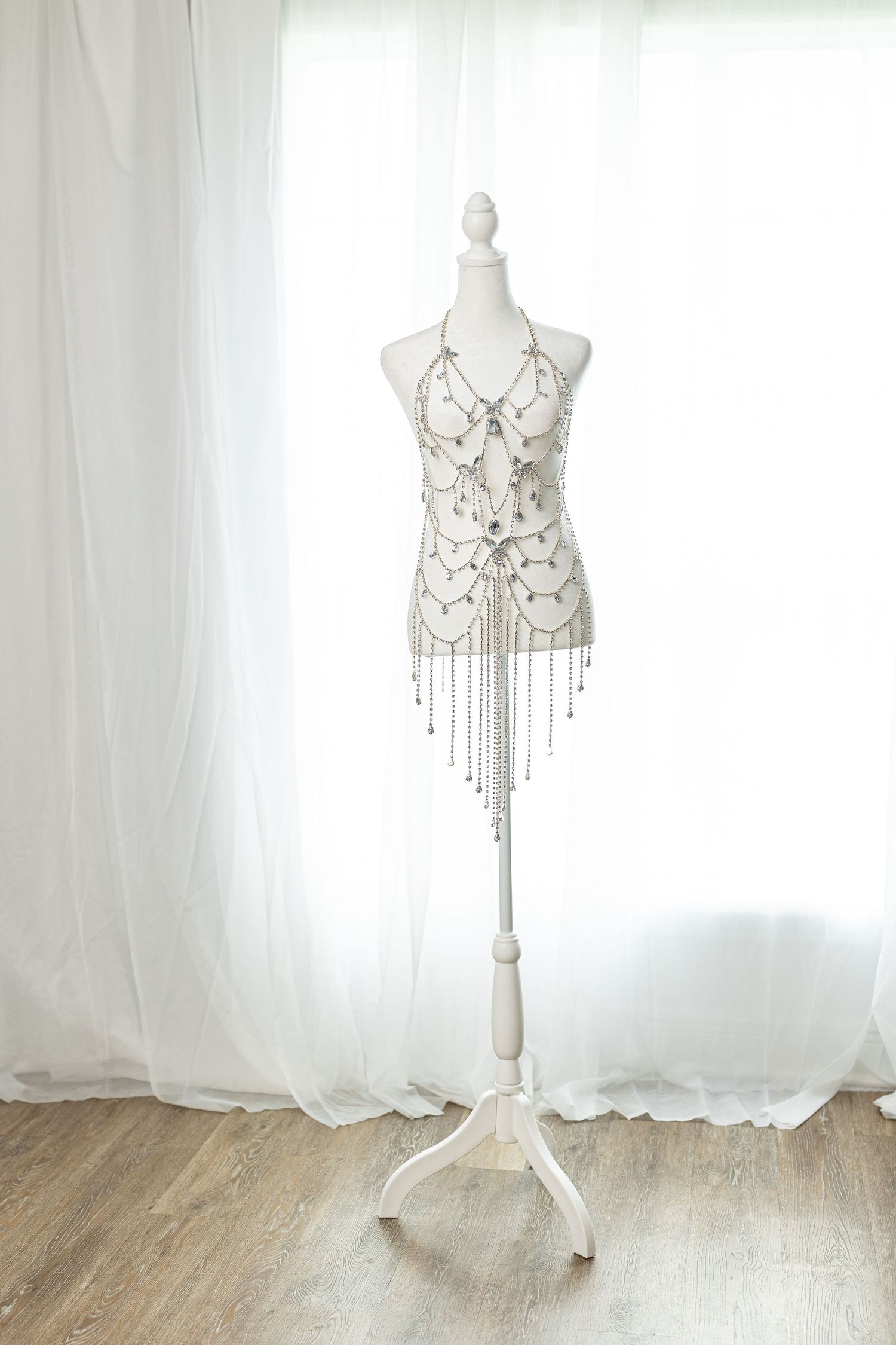 Elegant silver chain body jewelry displayed on a white mannequin stand against sheer white curtains.