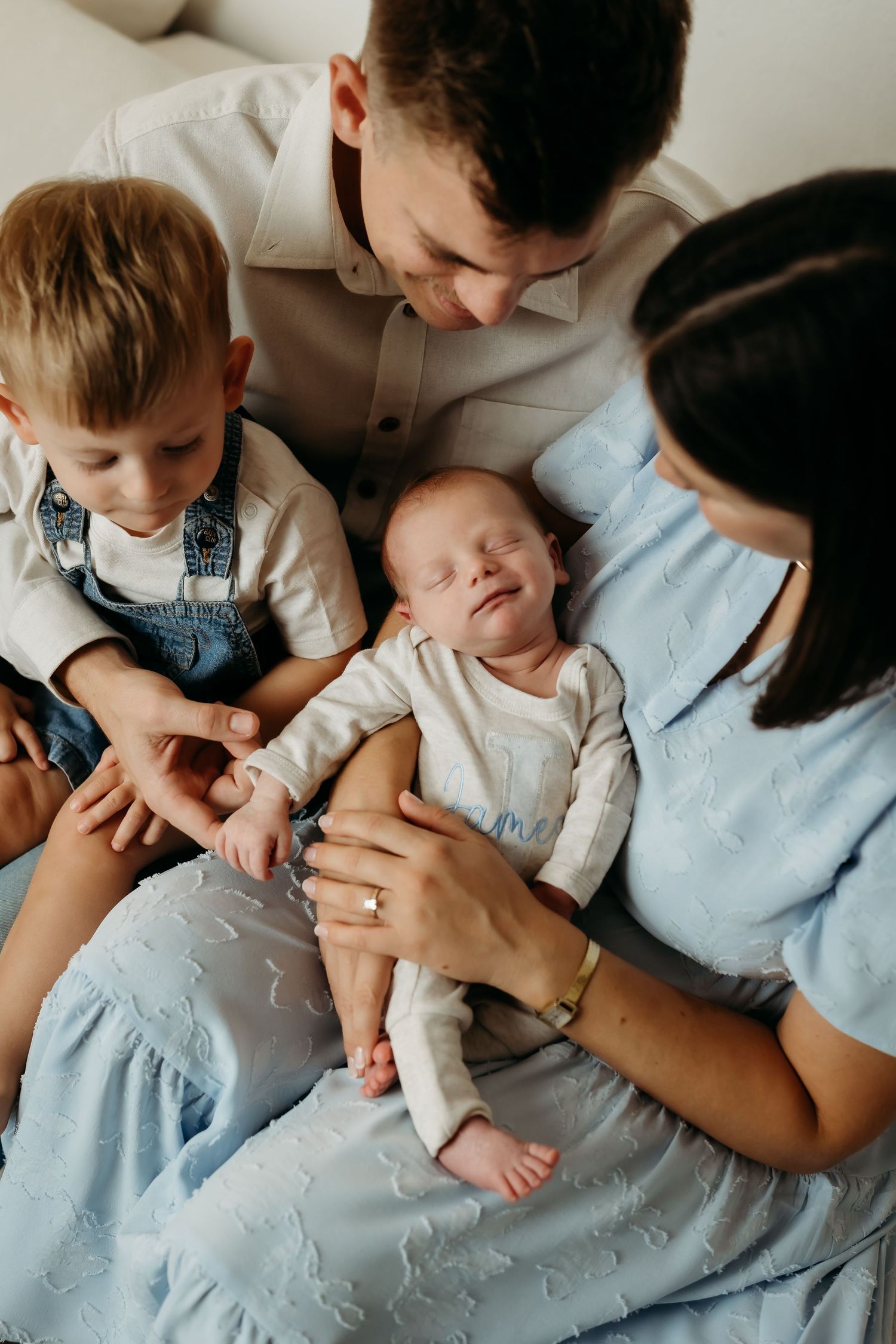 A loving family of four admires their sleeping newborn baby together in a bright, cozy room.