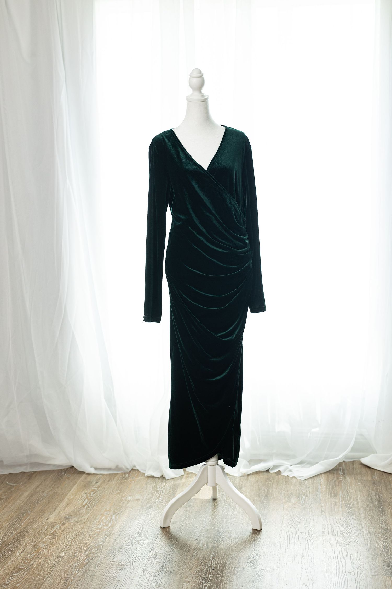 Dark green velvet long sleeve wrap maxi dress displayed on a white mannequin against sheer curtains.