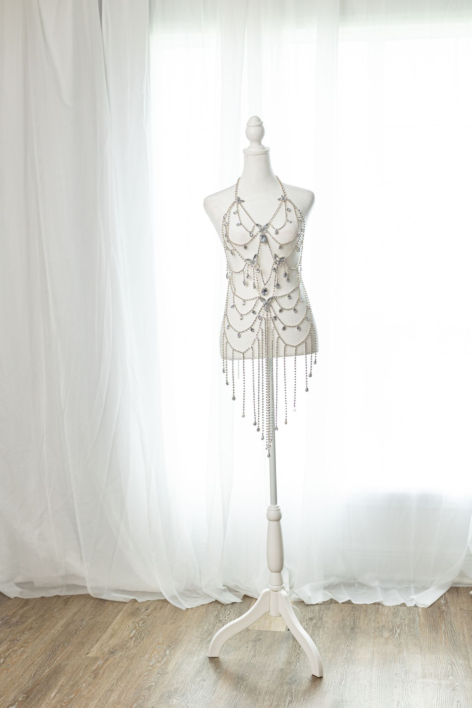 Silver beaded fringe halter top displayed on a white mannequin stand against sheer white curtains.