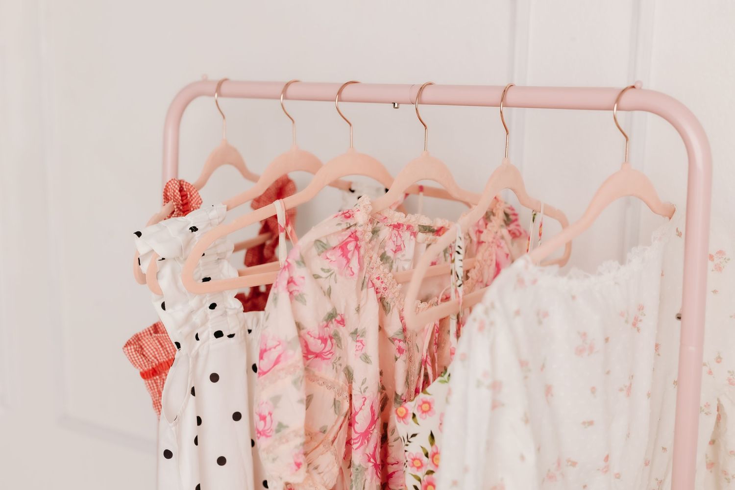Pink clothing rack displaying assorted floral and polka dot dresses on blush pink hangers.