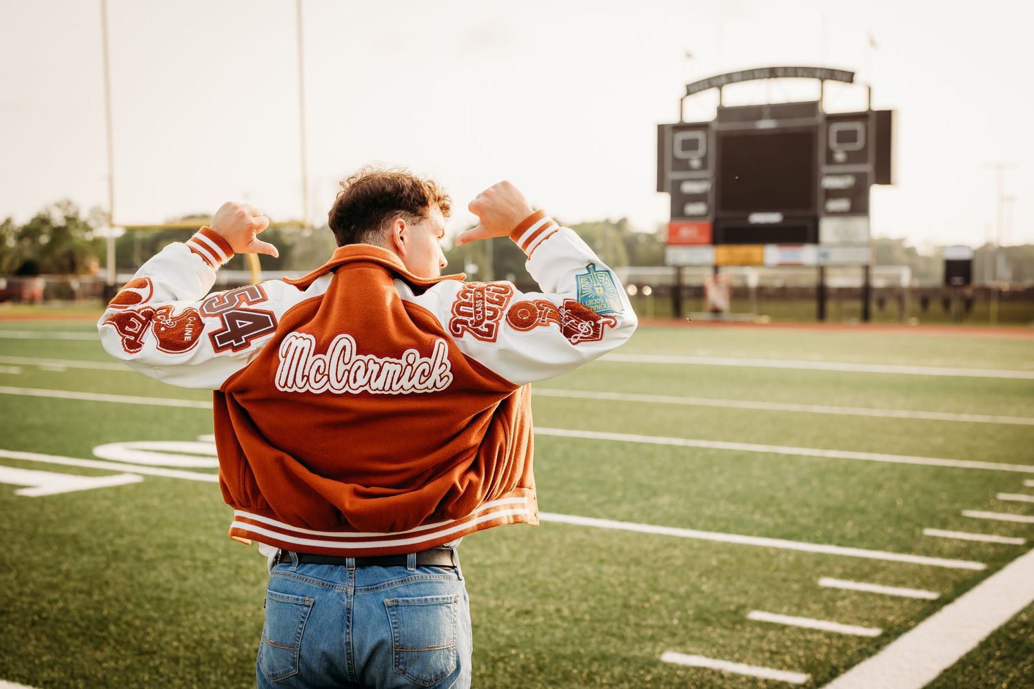 High school senior showing off his letterman jacket on a football field at his school.