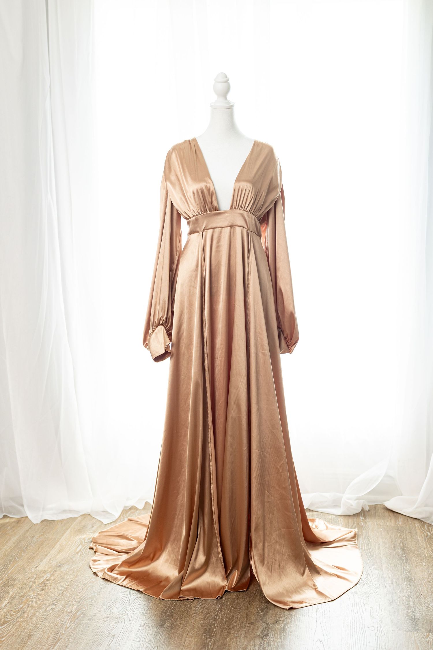 Elegant rose gold satin gown with deep V-neck, long sleeves, and flowing train displayed on a mannequin.