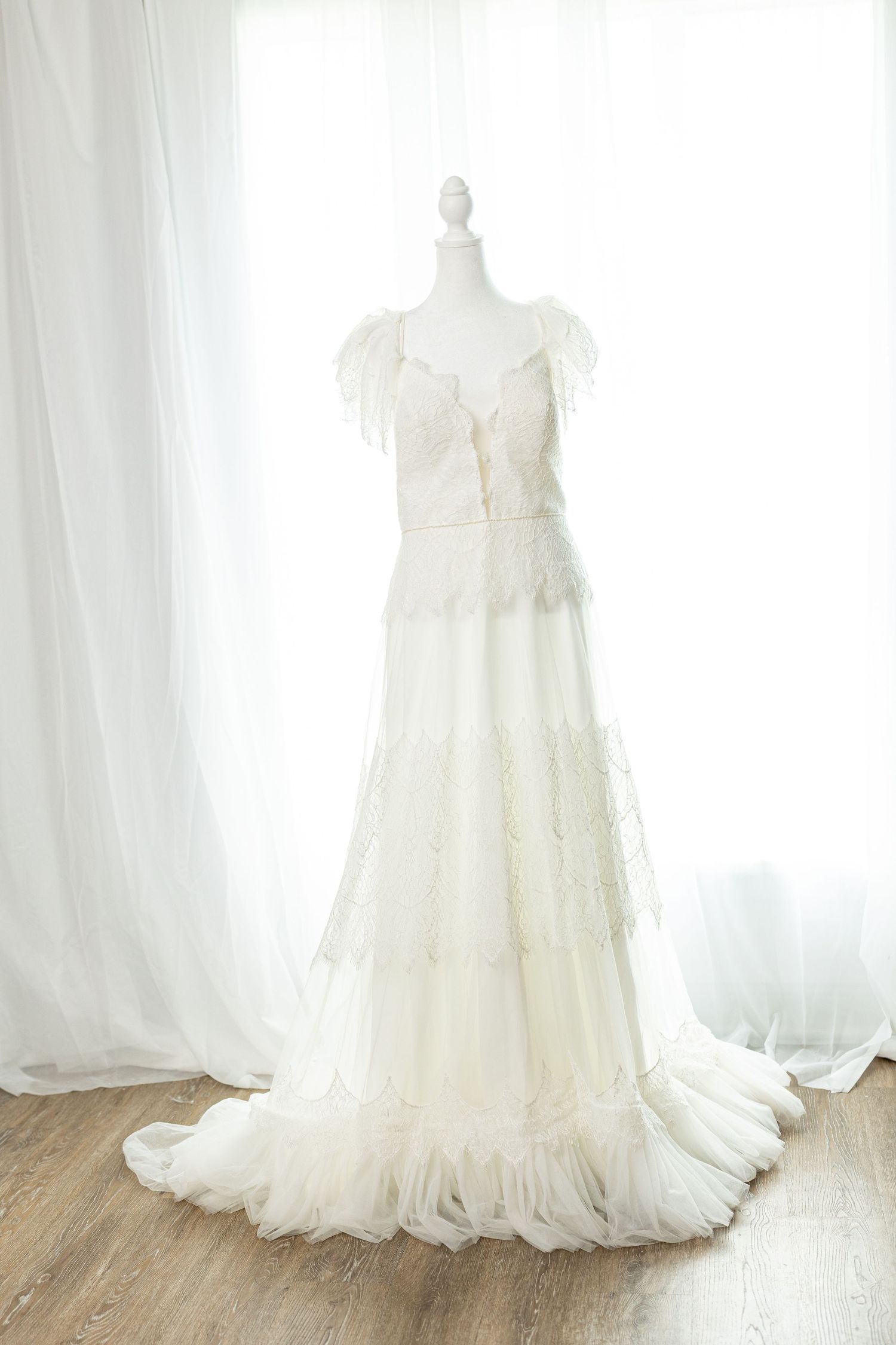 Elegant white lace wedding gown with ruffle details and flowing train displayed on a mannequin.
