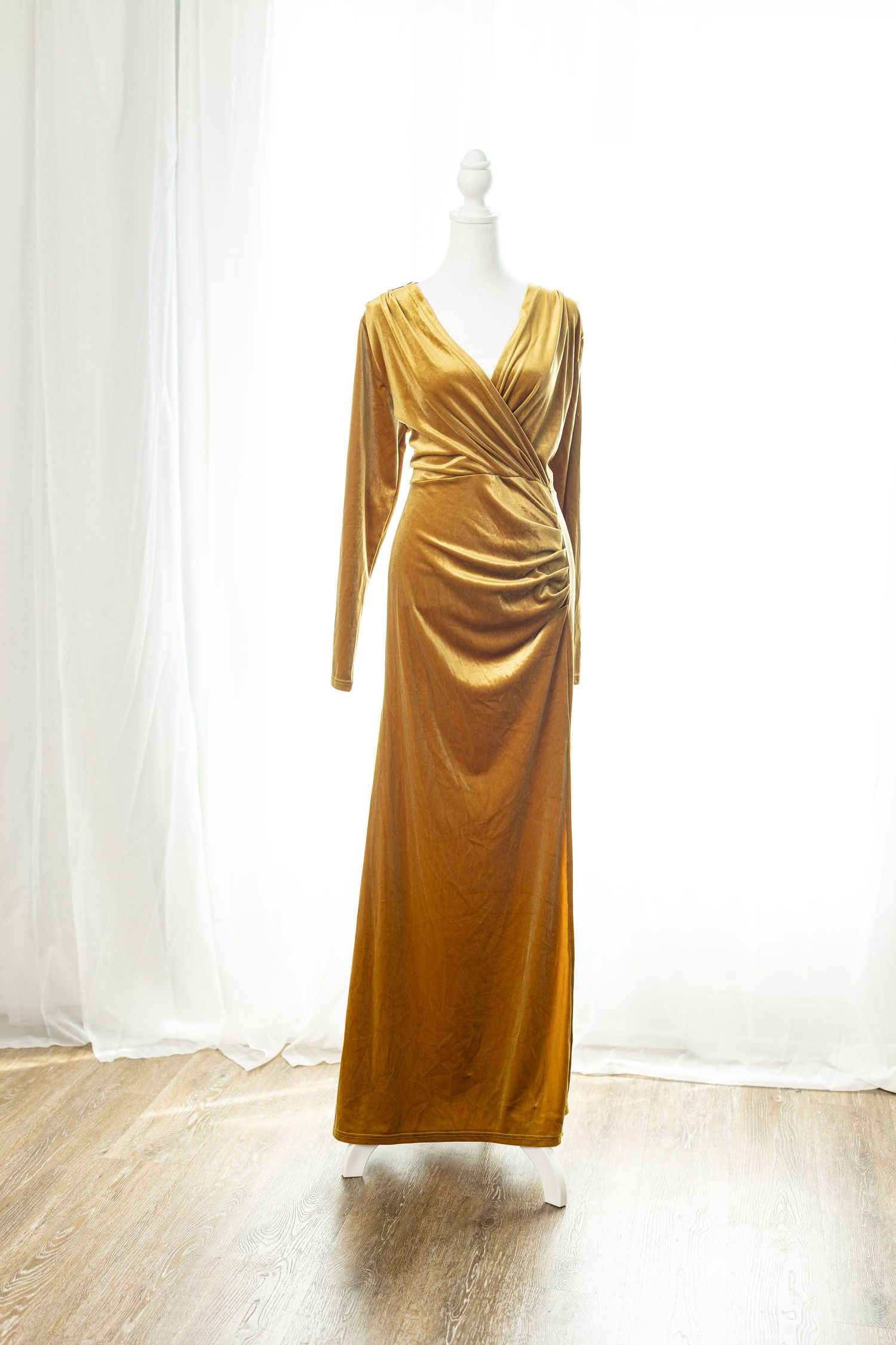 Gold velvet long sleeve wrap maxi dress on a white mannequin, featuring ruched waist detail and floor-length skirt.