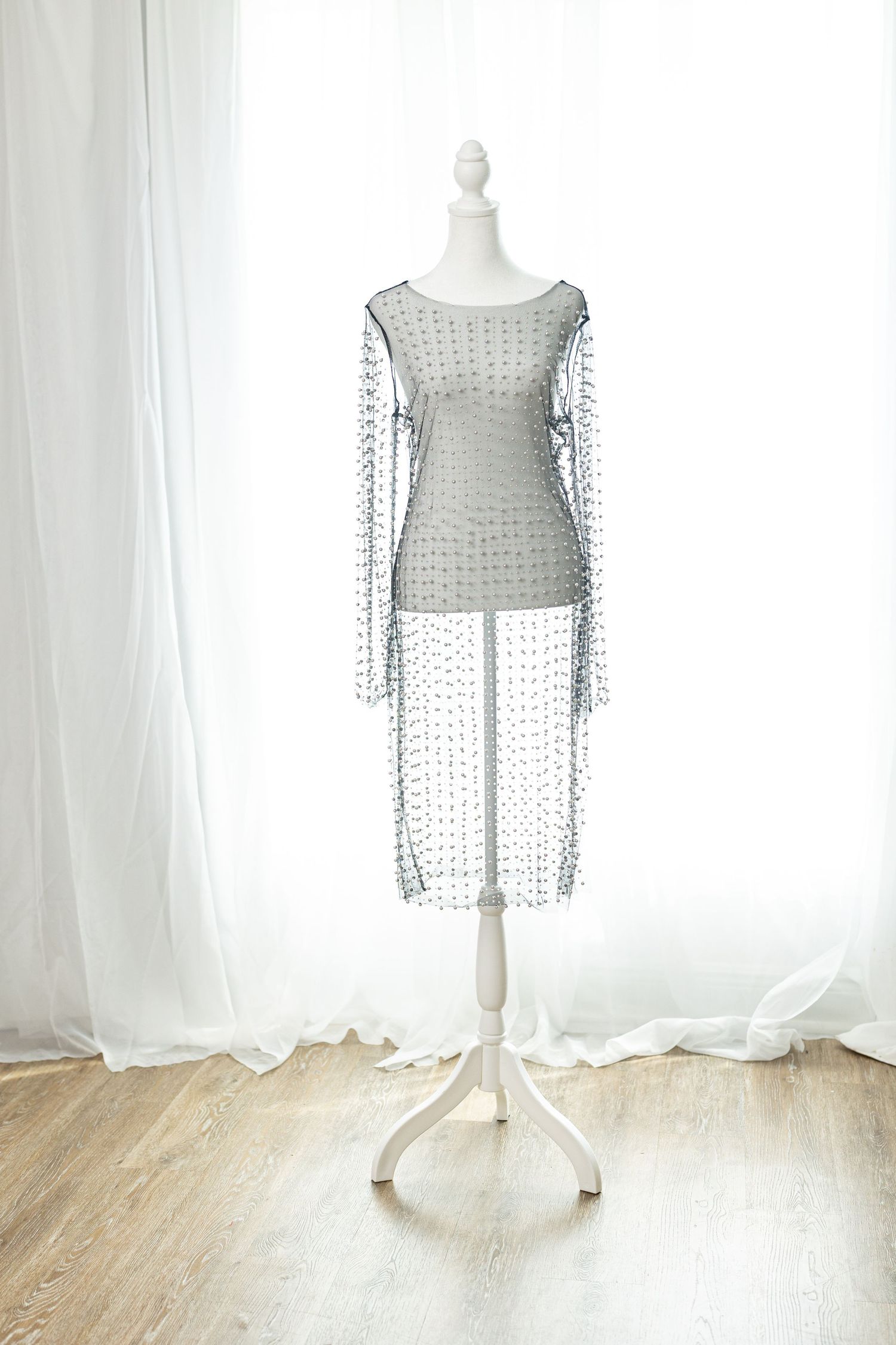 Sheer gray embellished long-sleeve mini dress with dot pattern displayed on white mannequin against white curtains.