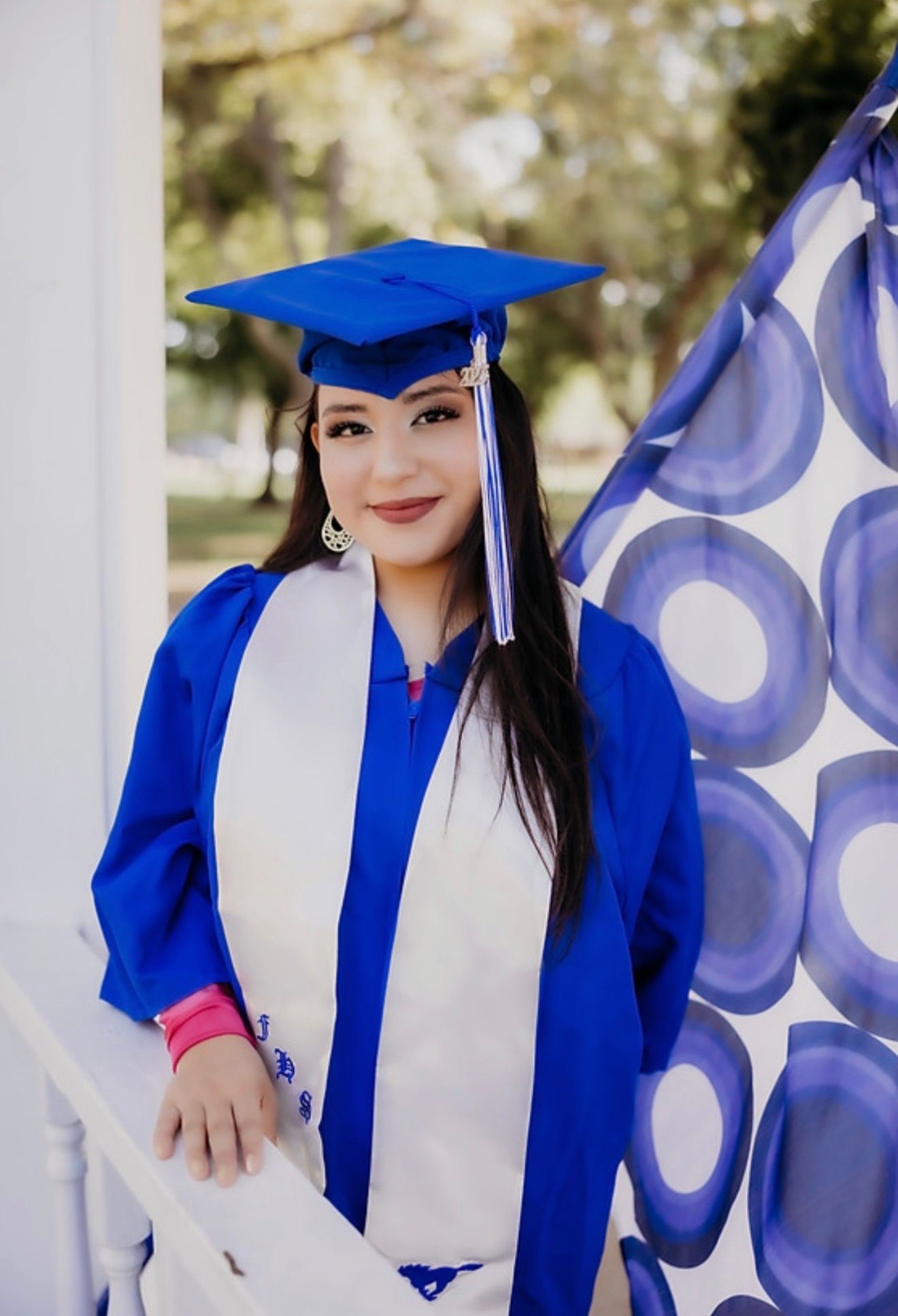 Female graduate in royal blue cap and gown poses outdoors for senior portrait photo.