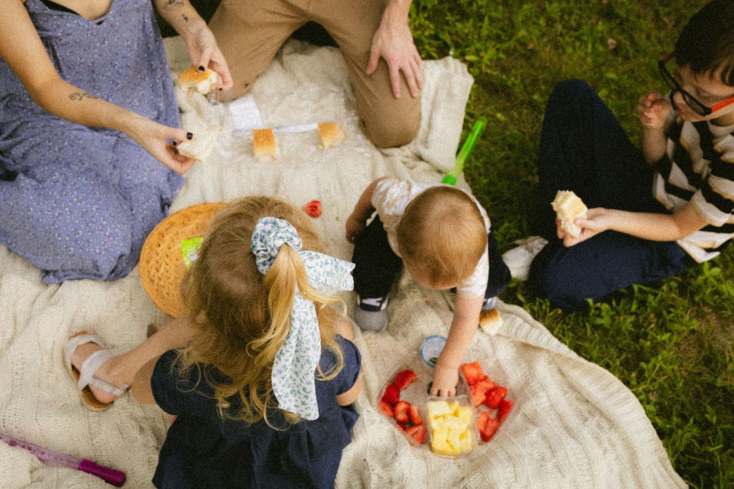 Family enjoying an outdoor picnic on a blanket in the grass, sharing food and snacks together.