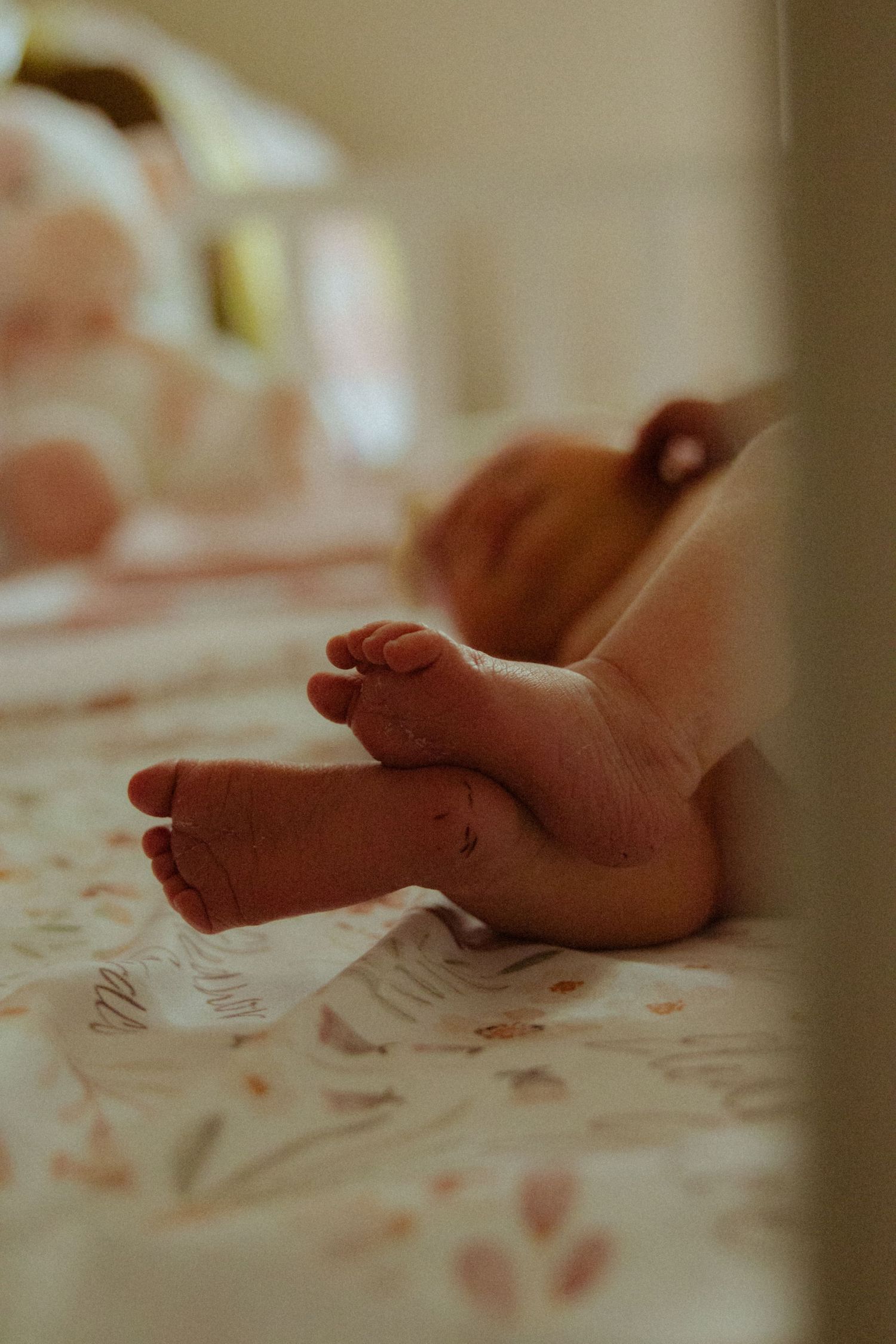 Newborn baby feet resting on a floral blanket in a soft-focus nursery setting.