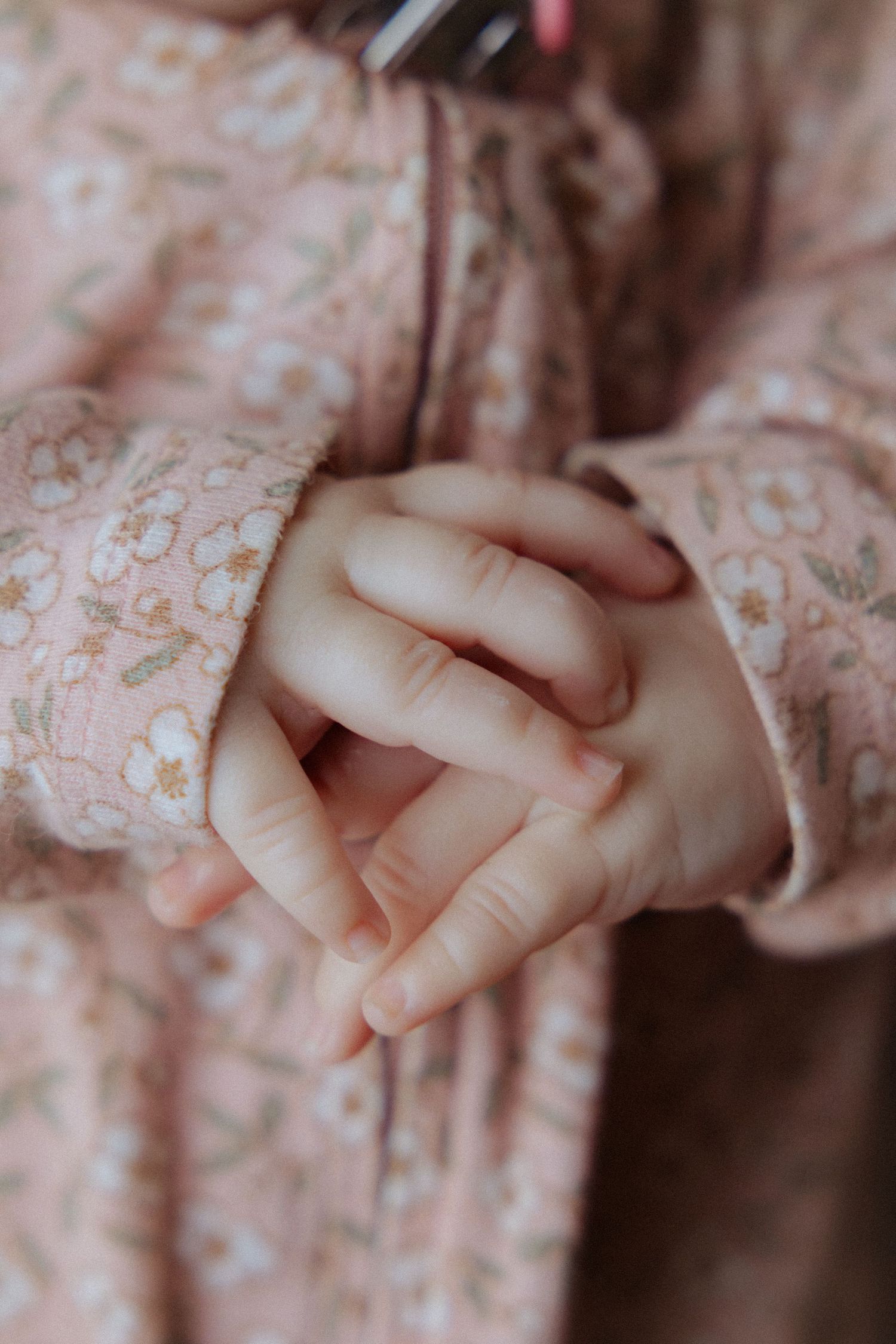 Close-up of a baby's clasped hands wearing a pink floral long-sleeve dress.