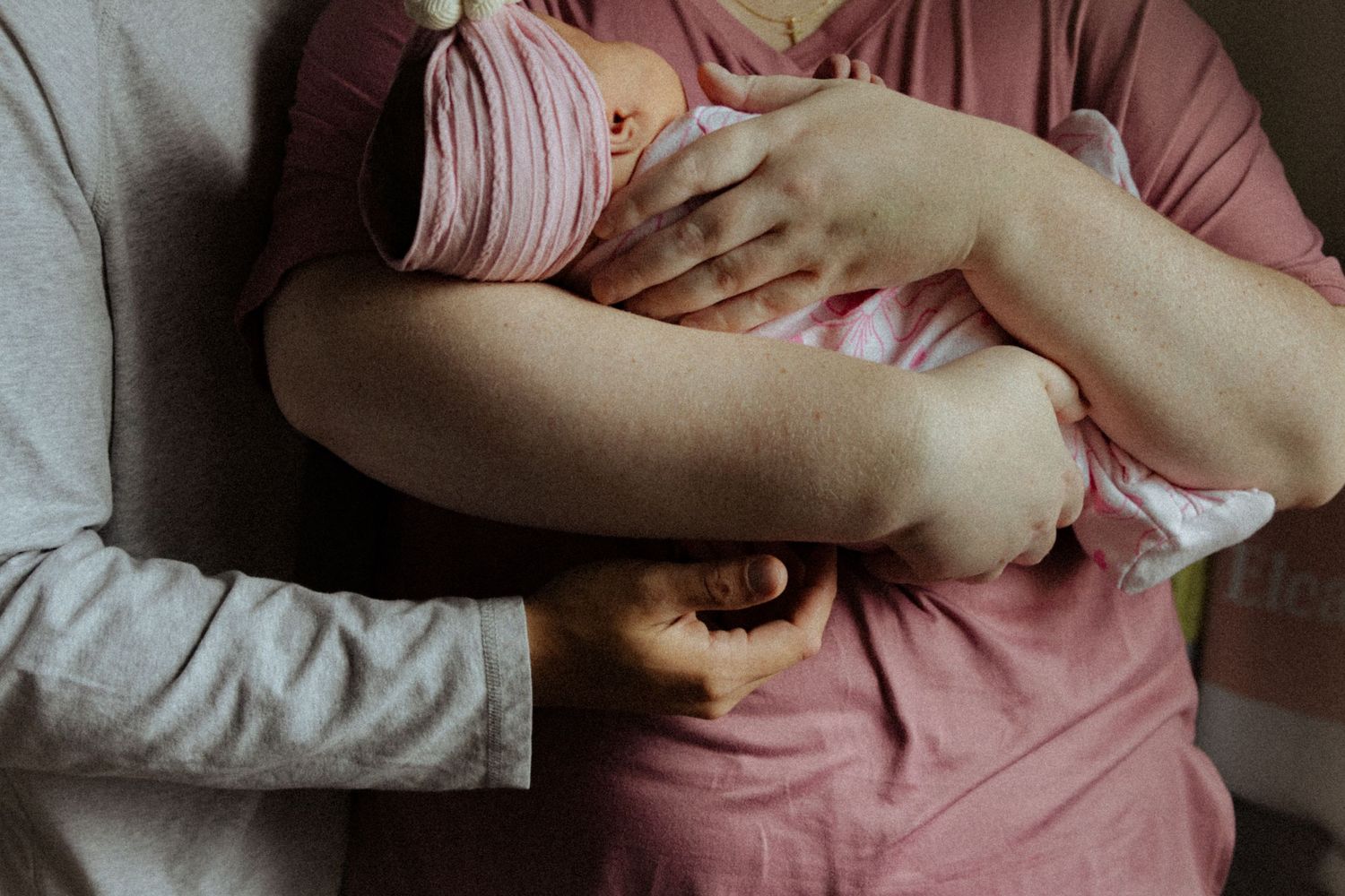 Parents cradling their newborn baby dressed in pink, sharing a tender family moment.