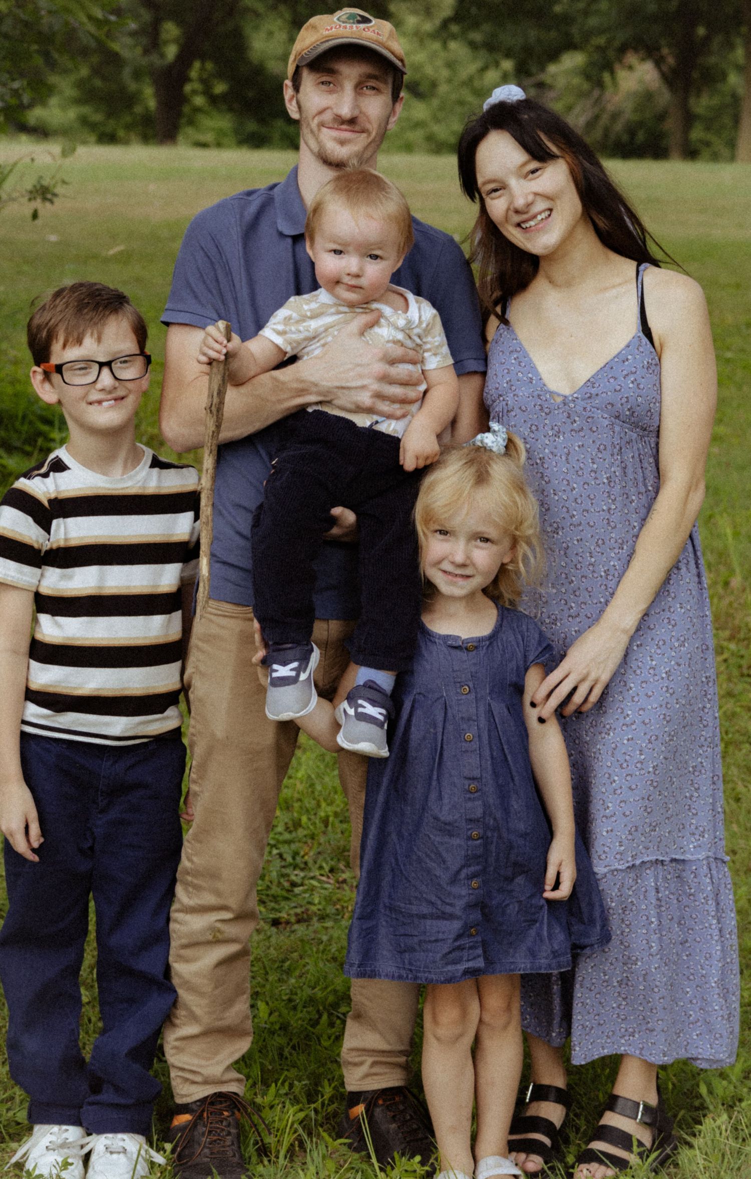 Happy family of five posing together on green grass in a sunny outdoor park.