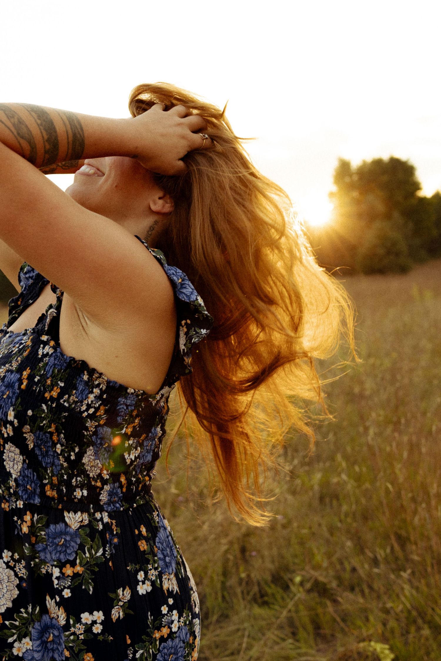 Woman in floral dress with long hair blowing in golden sunset light in a meadow field.