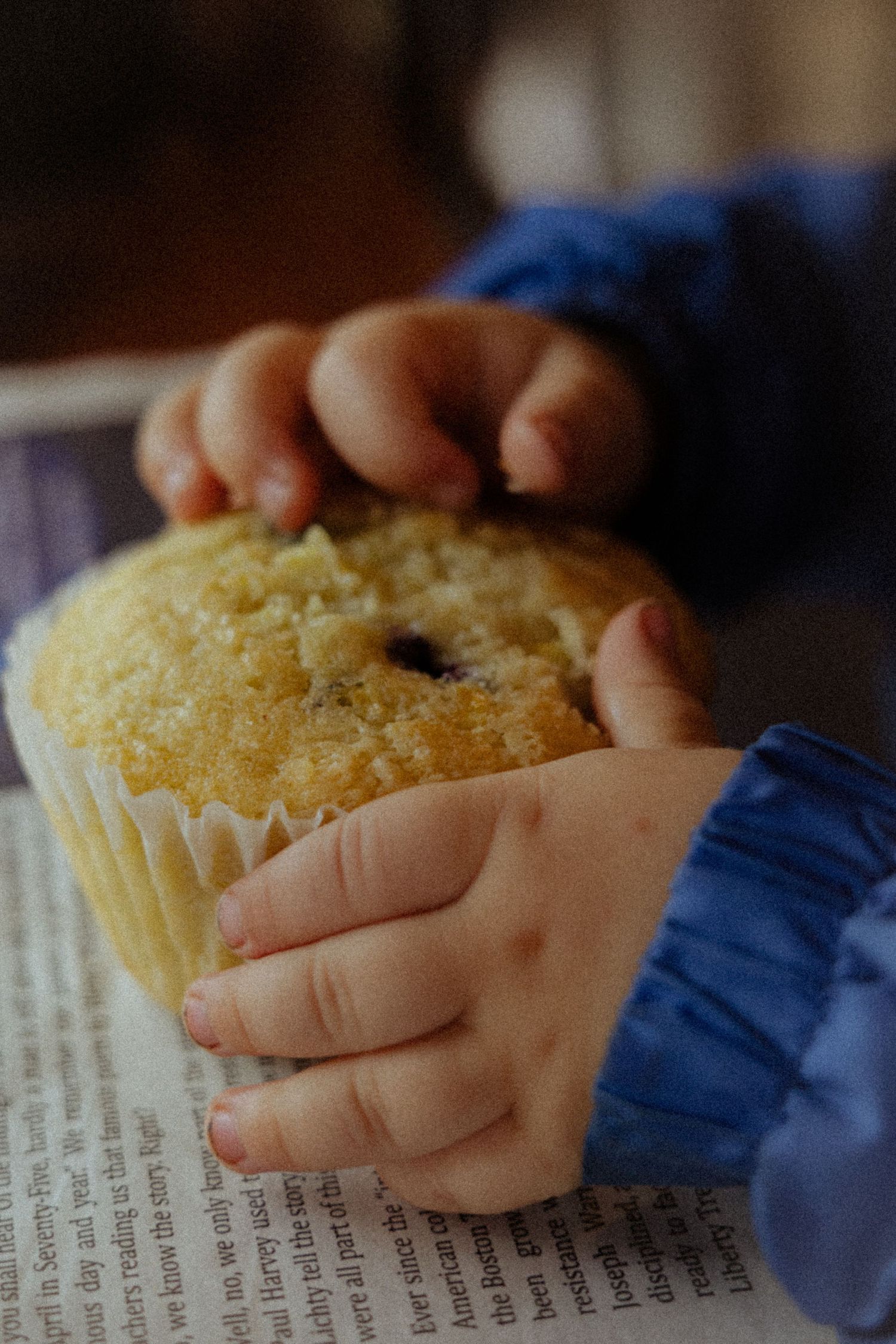 Small child's hands holding a blueberry muffin over an open book.