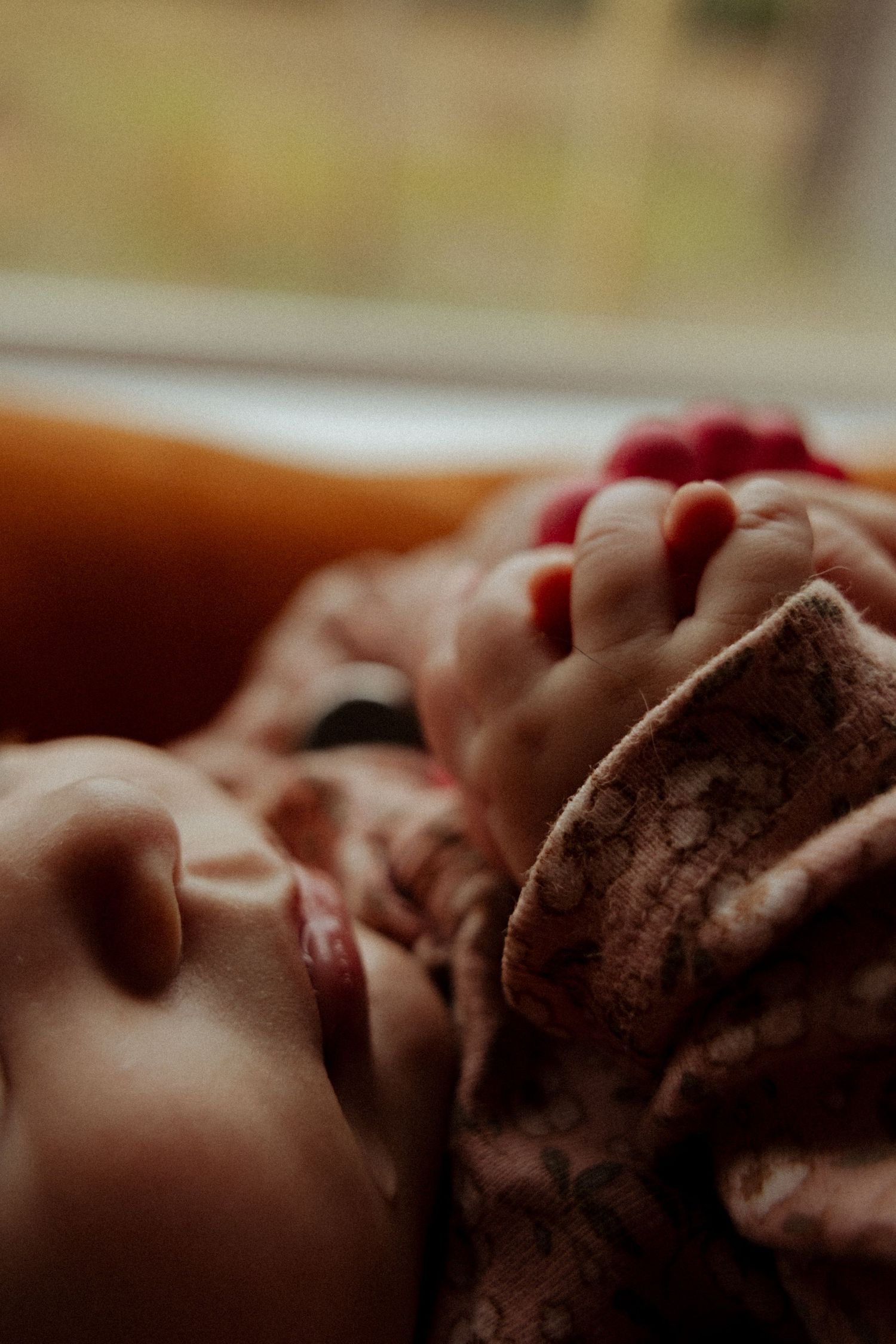 A sleeping newborn baby wrapped in a soft floral blanket, with tiny fingers visible near their peaceful face.