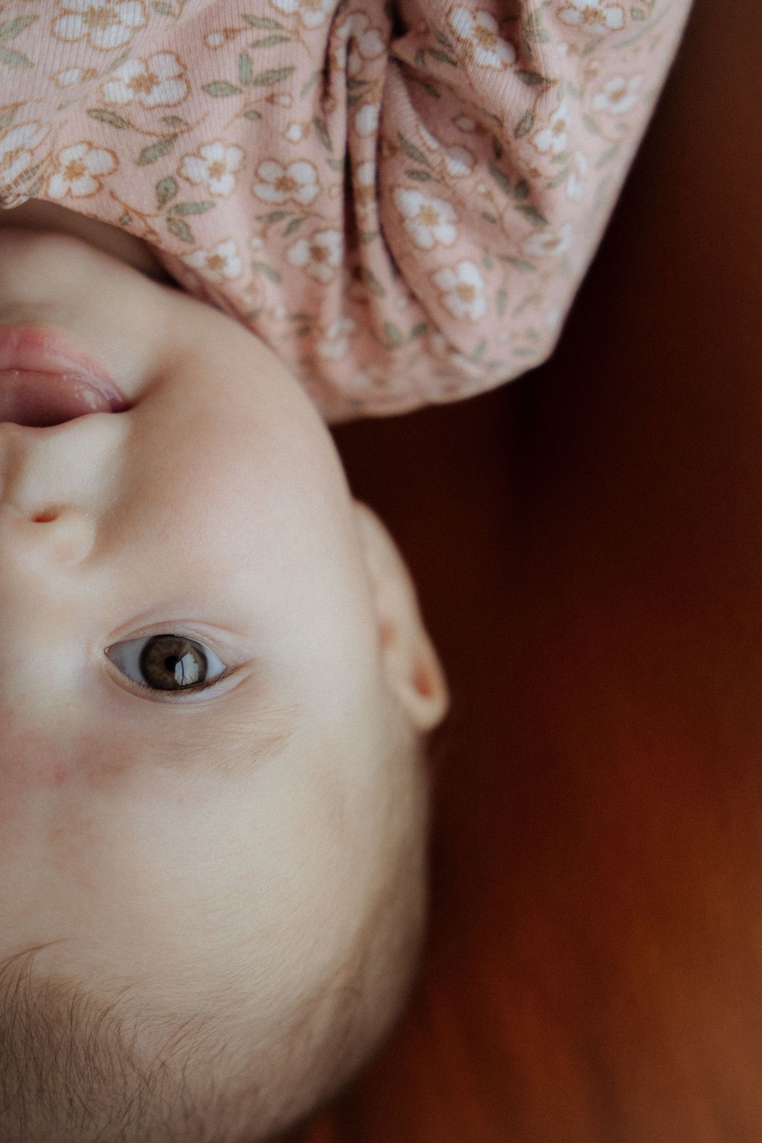 Close-up of a baby's face upside down wearing a pink floral headband.