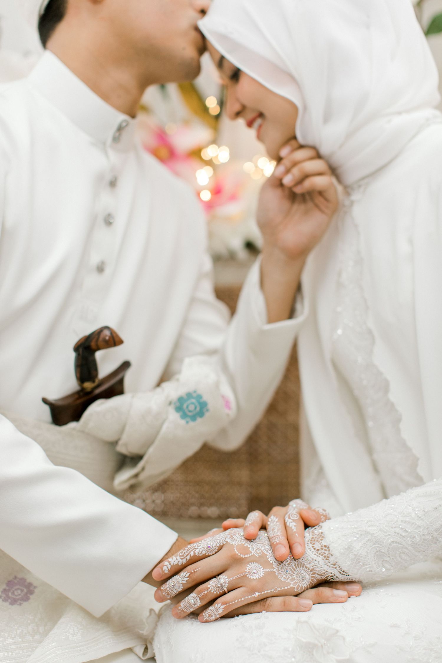 Malaysian  bride with white henna hands smiling at groom during traditional Malay wedding ceremony.