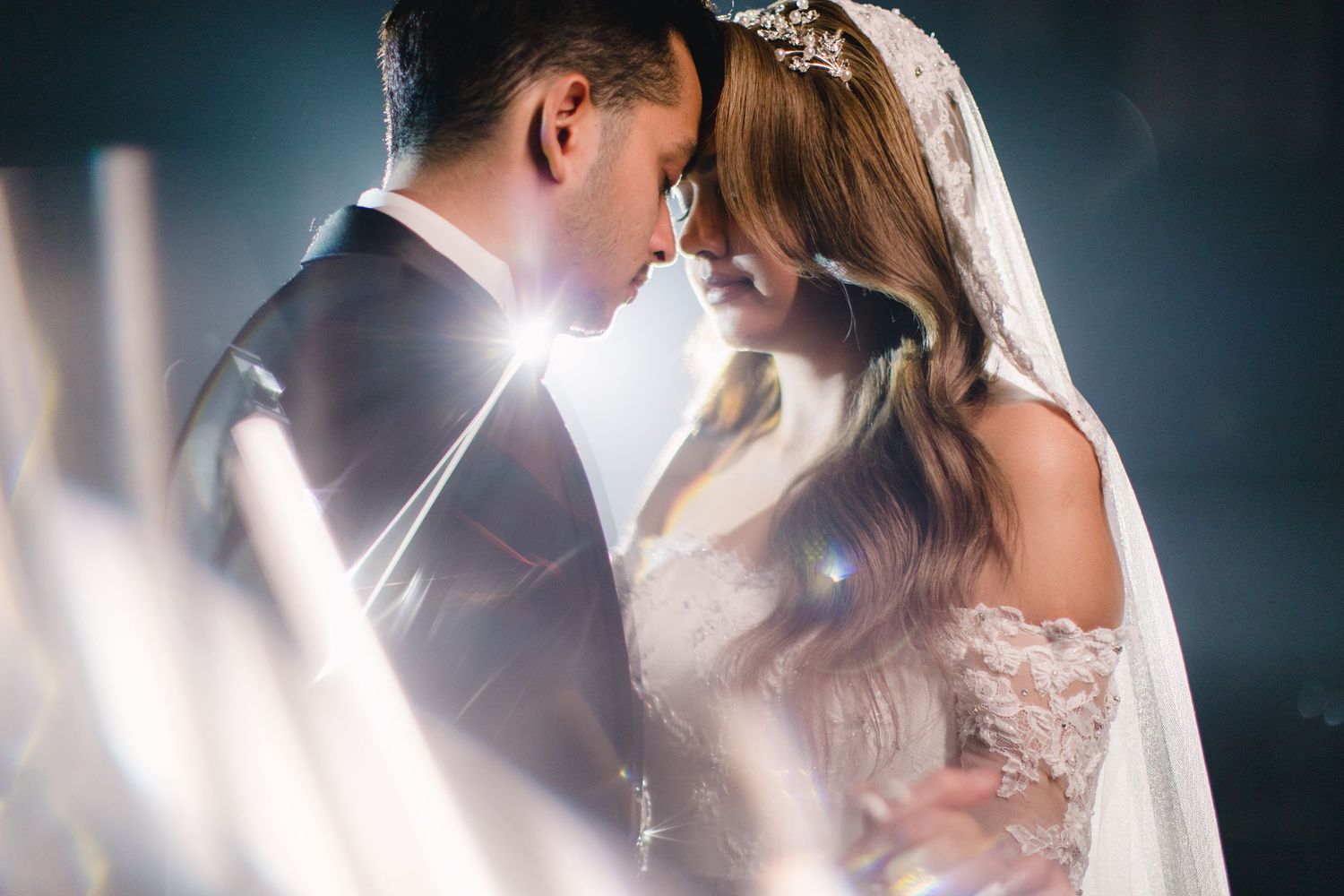 Bride and groom in elegant wedding attire sharing an intimate moment surrounded by sparkling light effects.