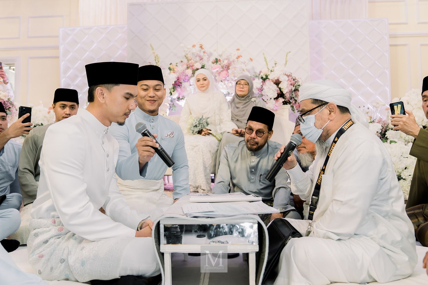 Malaysian groom signing wedding documents at the akad nikah ceremony surrounded by family and guests.