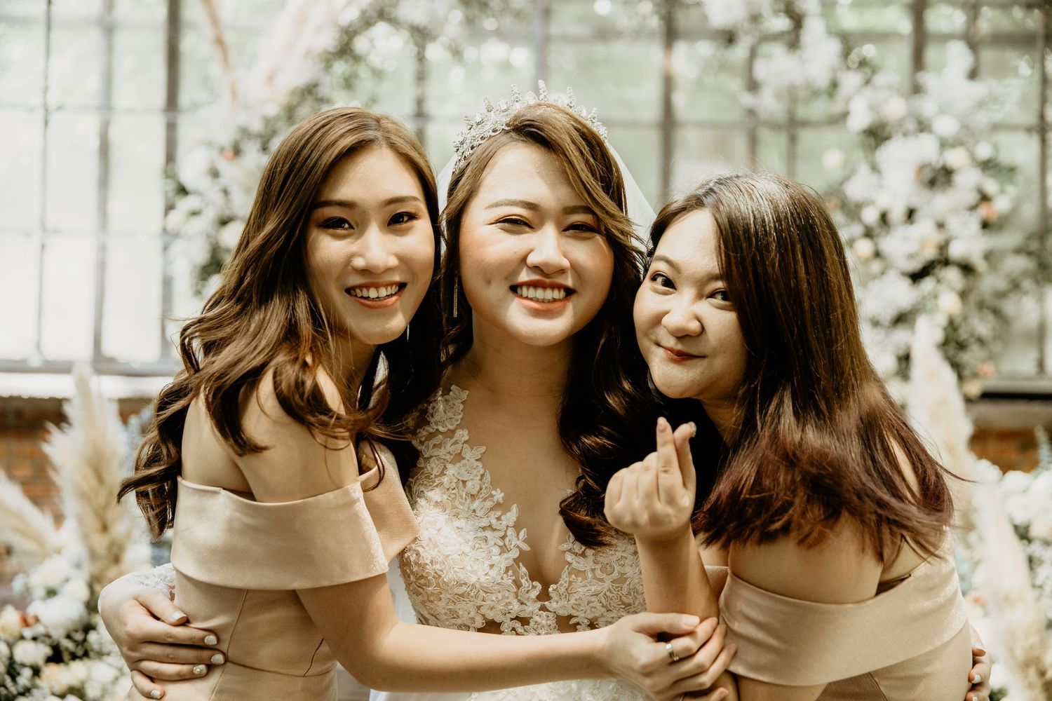 Smiling bride wearing tiara poses with two bridesmaids in champagne dresses at wedding reception.