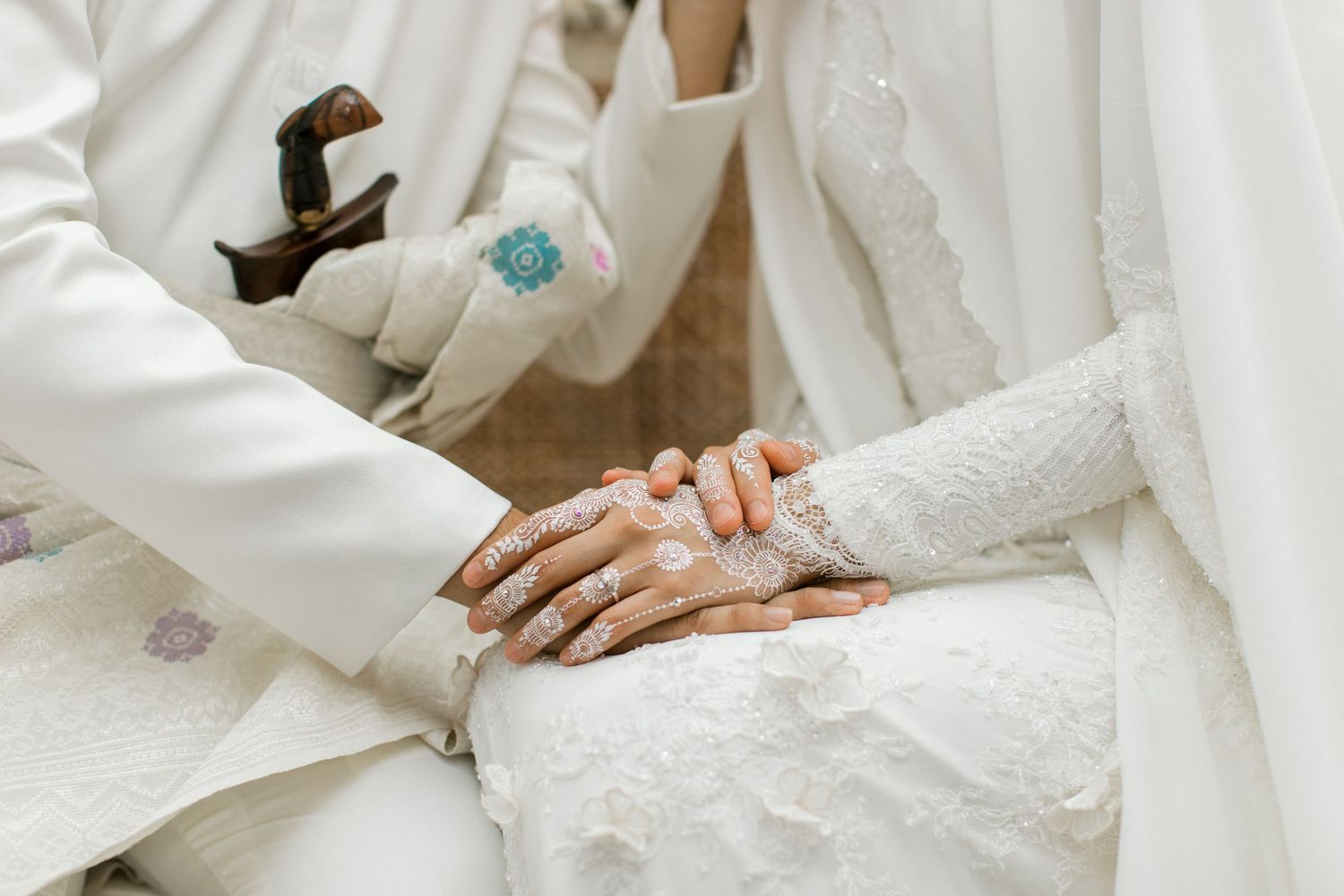 Bride and groom in white attire holding hands with henna detail during a traditional wedding ceremony.