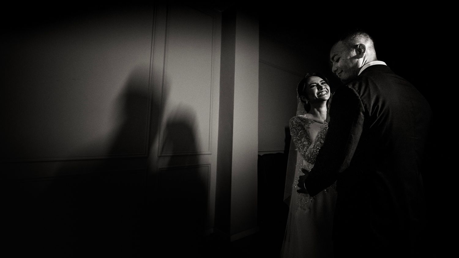 Black and white wedding photo of a couple embracing with dramatic shadows on the wall behind them.