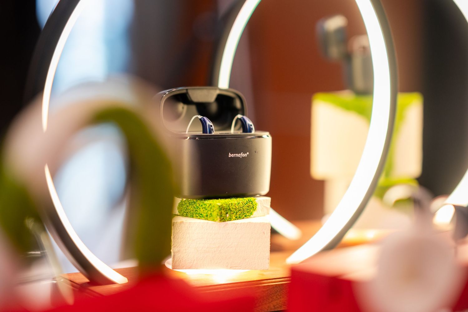 Wireless earbuds in charging case displayed on moss pedestal with circular LED light.